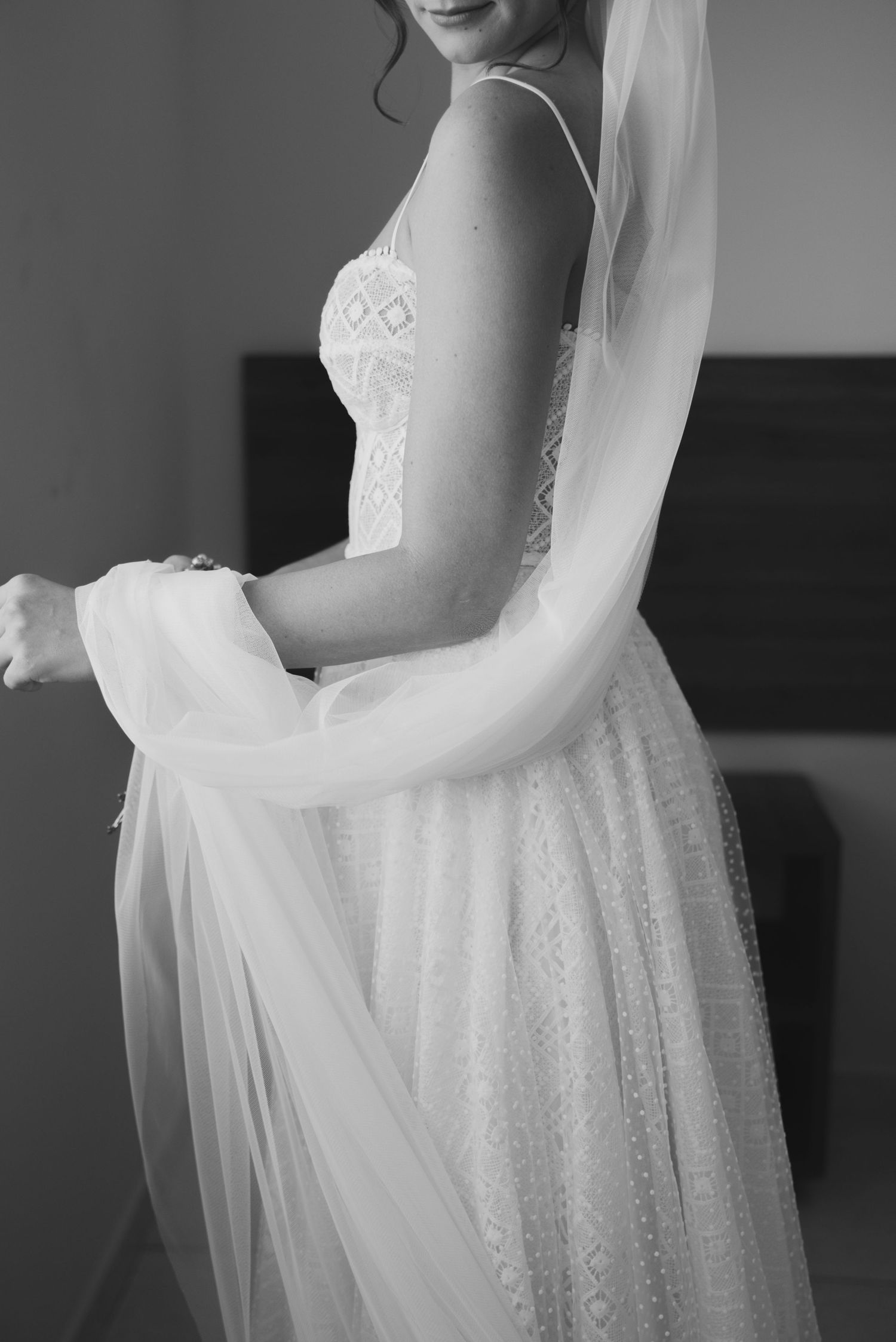Black and white detail of lace wedding dress with flowing veil.