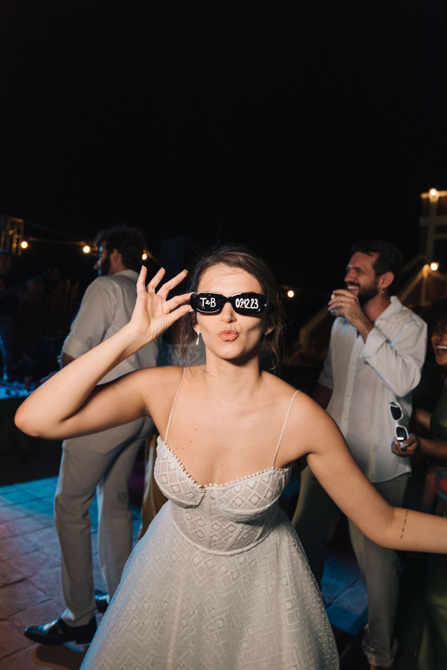 Person in white dress and sunglasses dancing at a nighttime celebration.