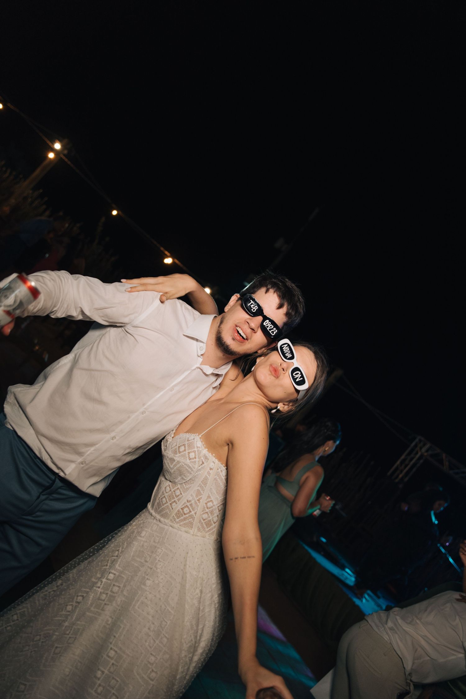 Couple wearing sunglasses while dancing together at an outdoor evening reception.