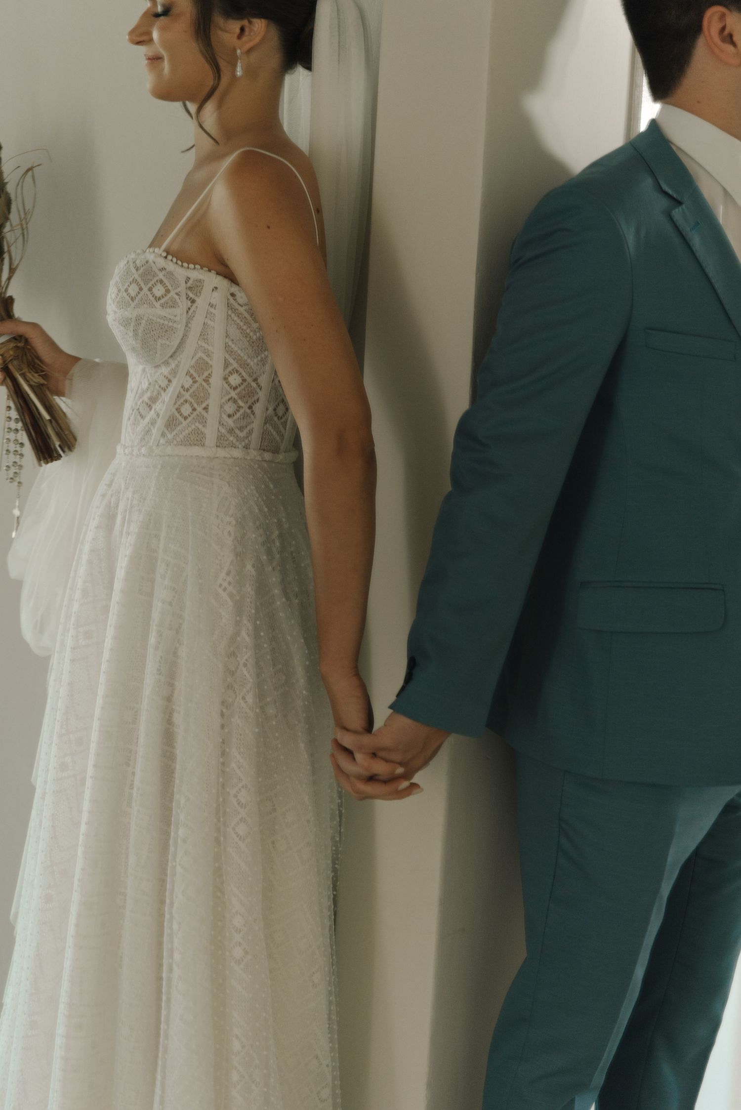 Bride and groom hold hands in first look moment, showing dress details and teal suit.