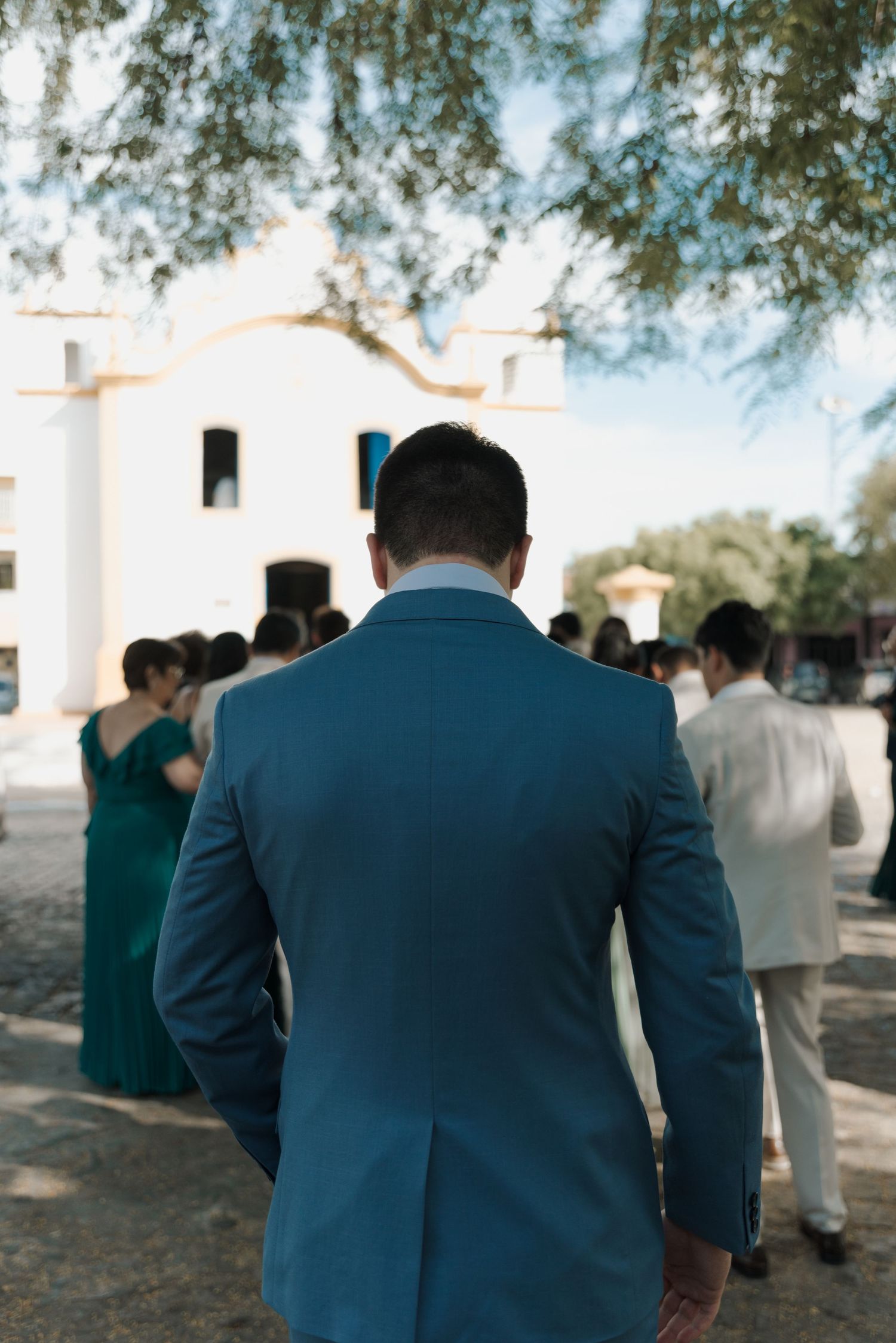 Groomsman in blue suit watching wedding ceremony outside white church.