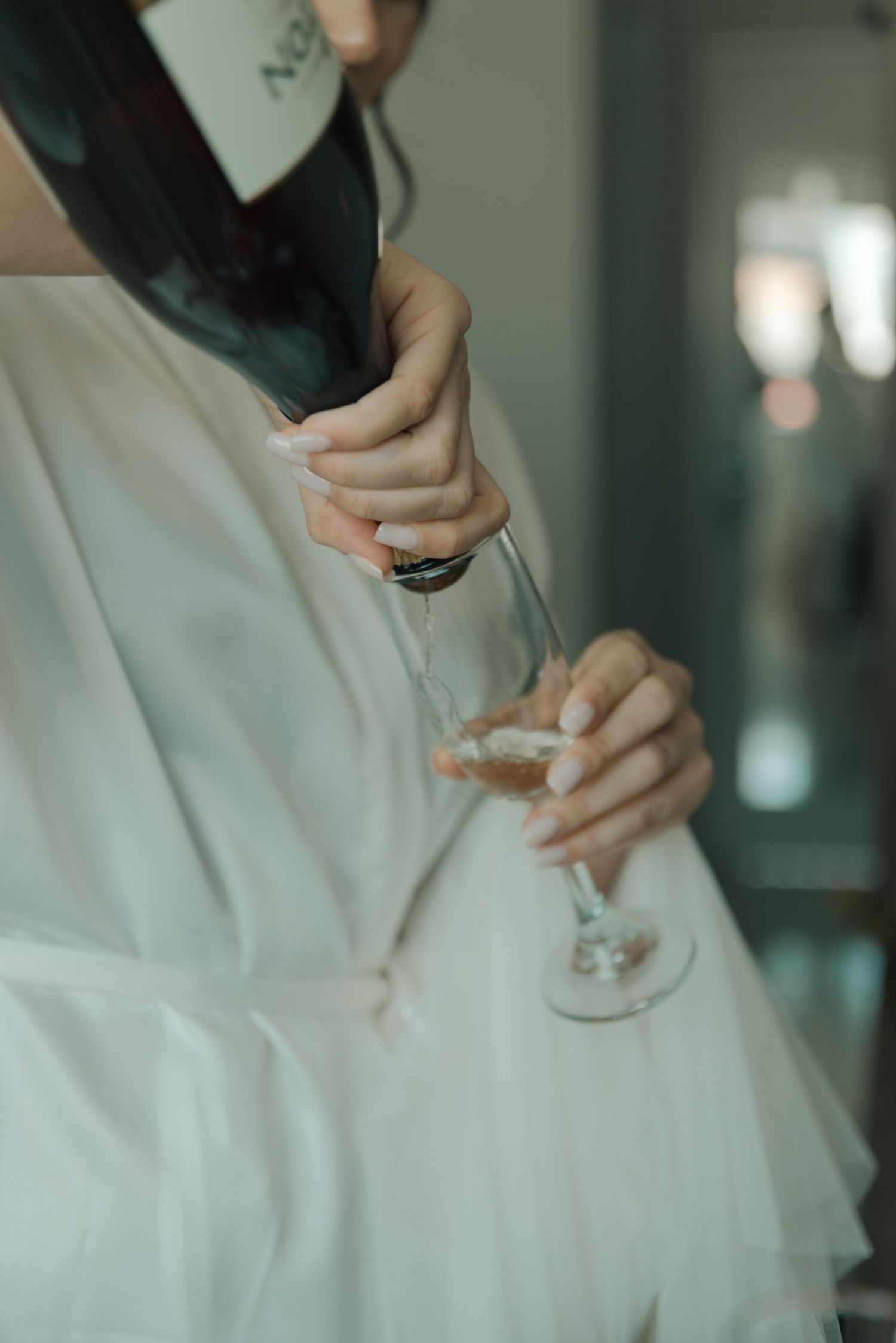 Hands pouring champagne into a glass while wearing a white bridal robe.