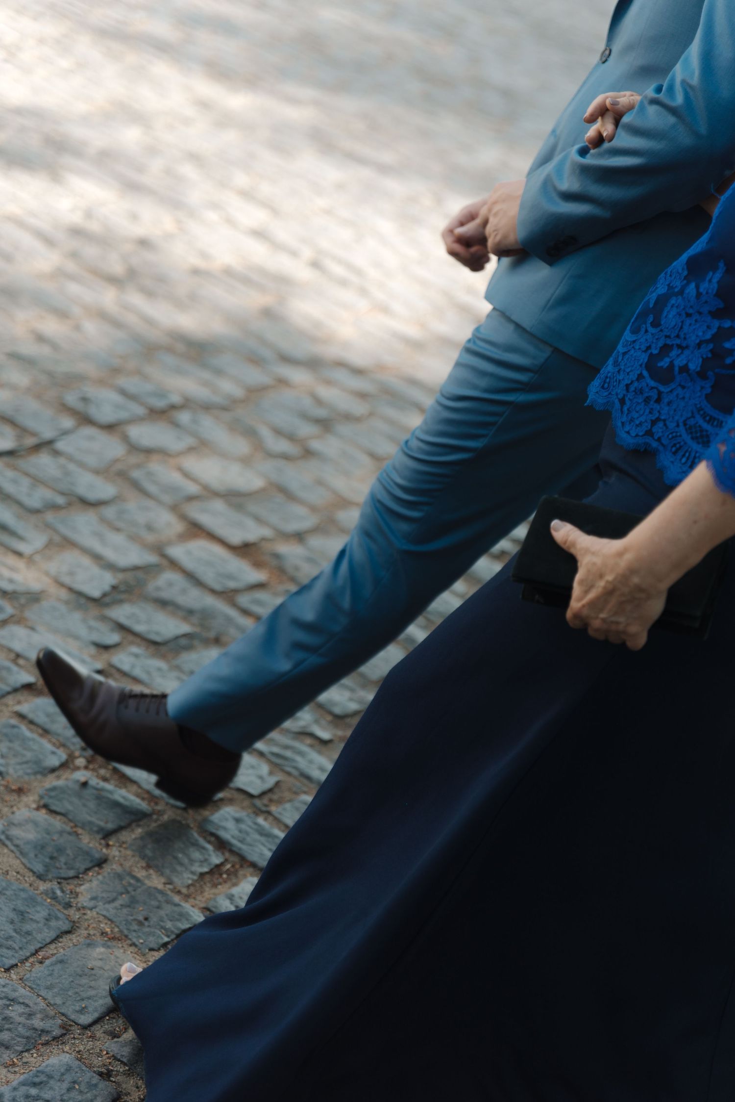 Close-up of formal attire and cobblestone ground at outdoor wedding.