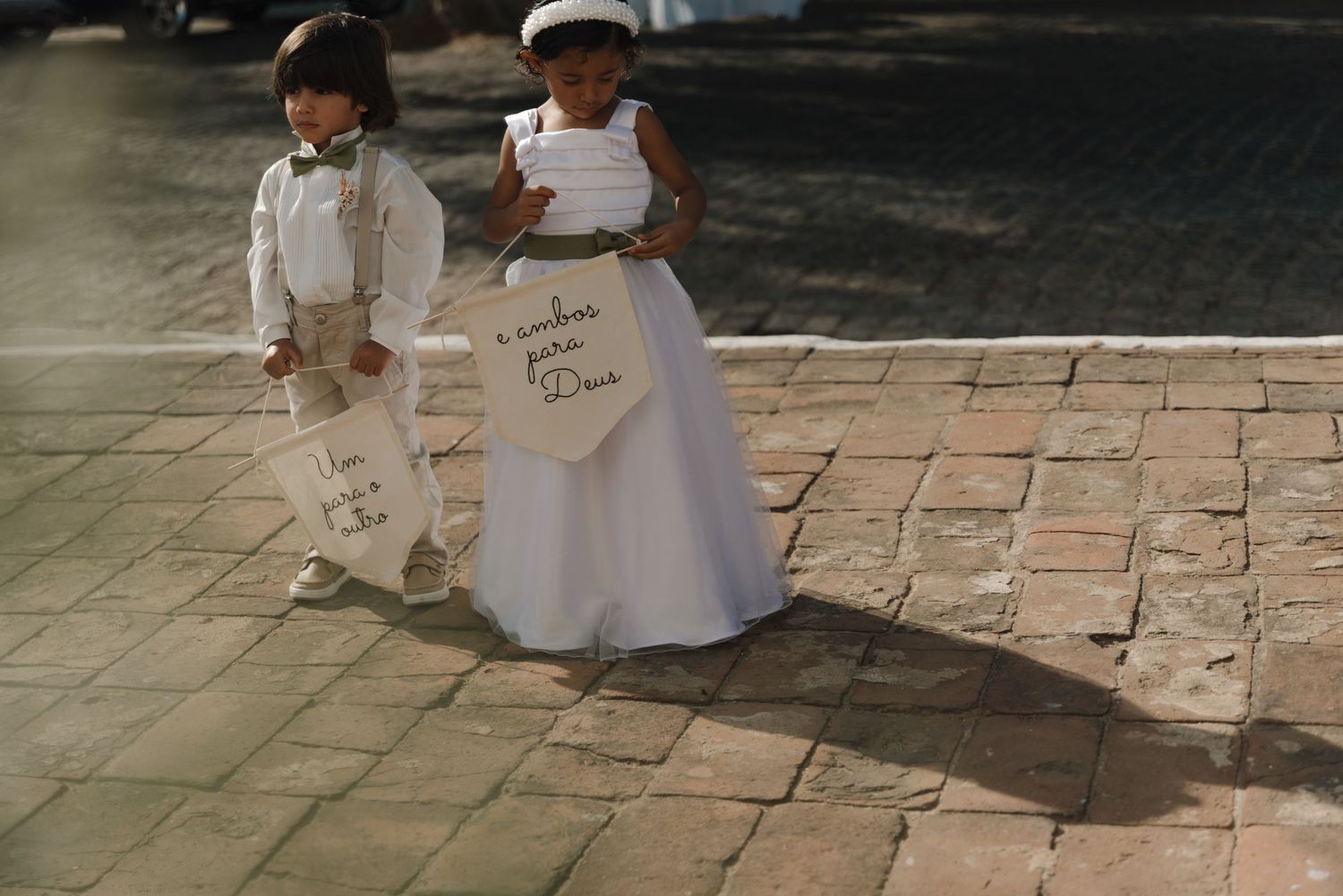 Two children in wedding attire holding paper signs on stone pavement.