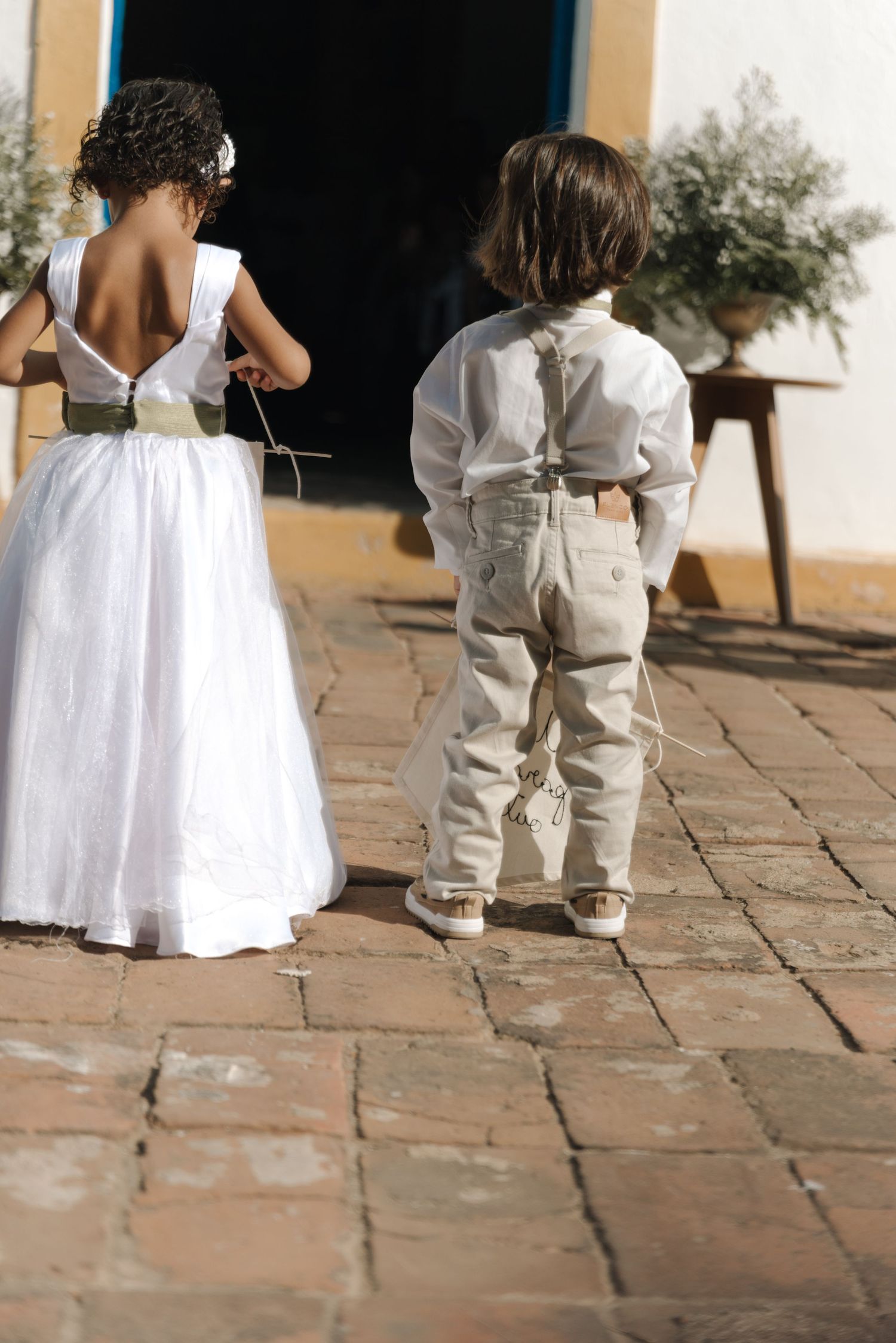 Children in white dress and suspender outfit stand outside church entrance.