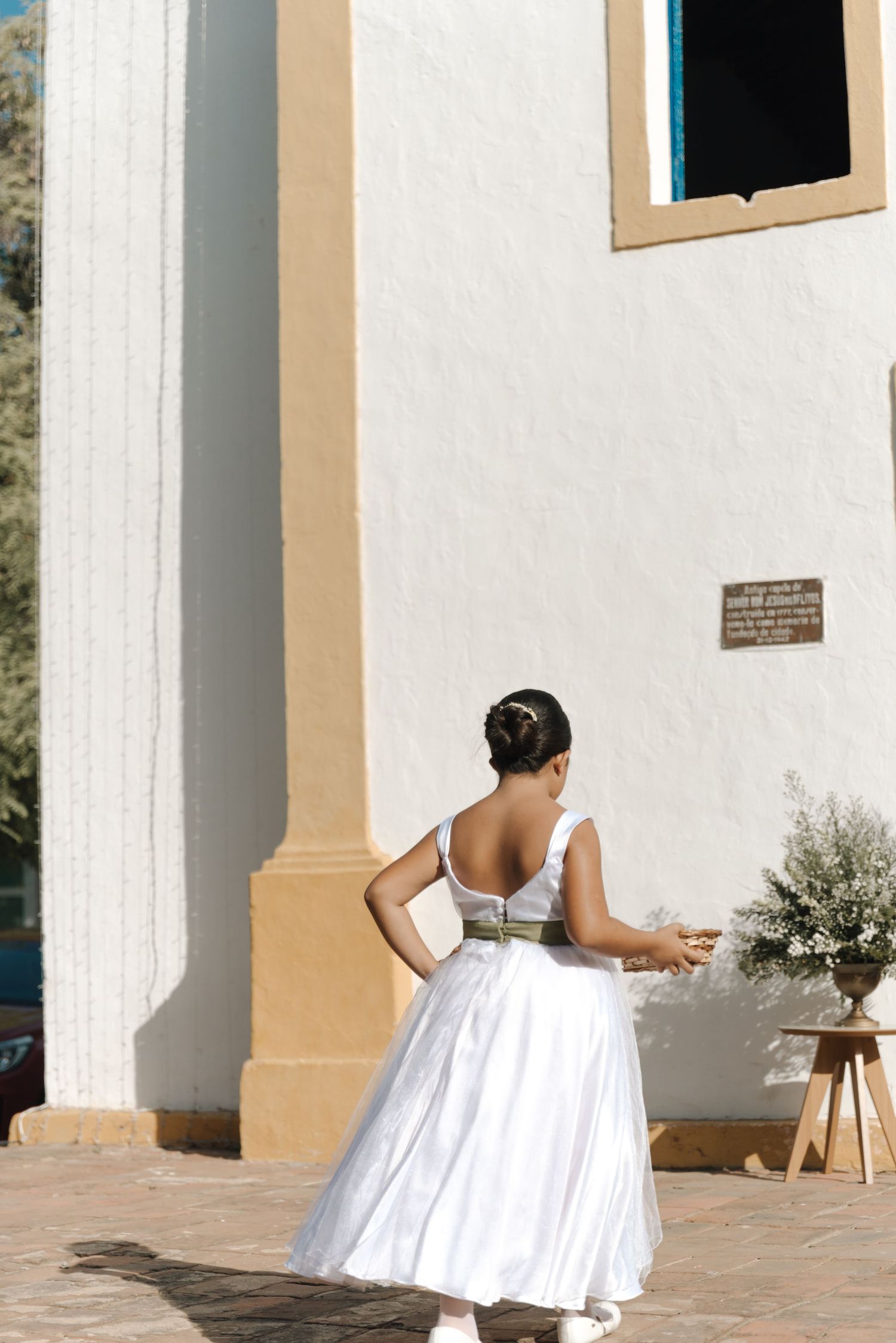 A person in a white wedding dress stands outside a white church with ornate tan trim and a blue door.