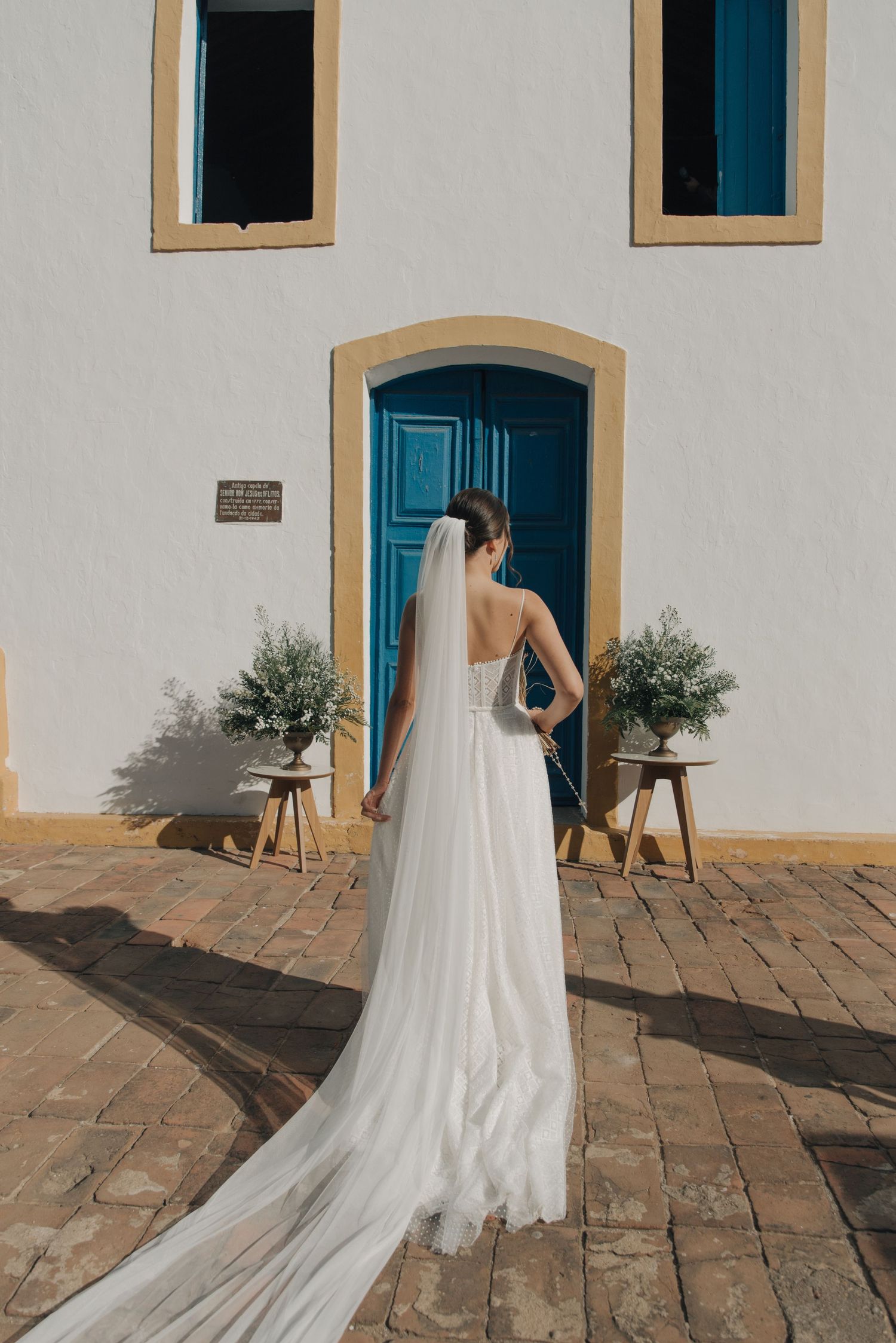 A bride in a flowing white gown and long veil stands before a turquoise church door.