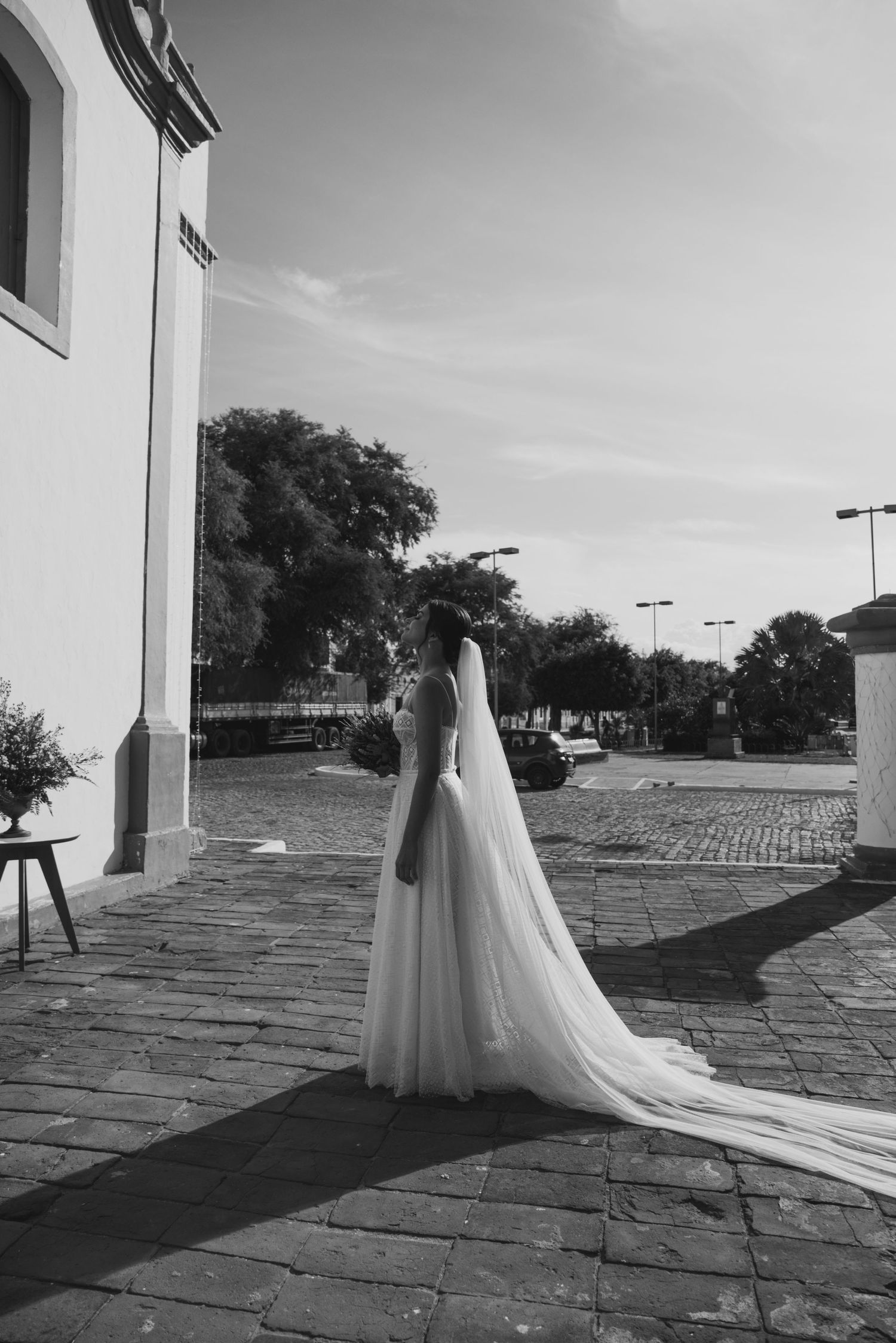 Black and white photo of a bride in a flowing dress standing on cobblestone pavement.
