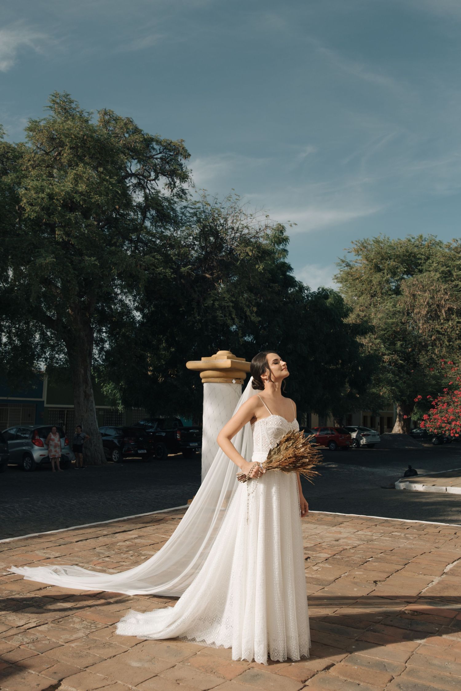 A bride in a flowing white gown holds dried flowers outside a historic church.