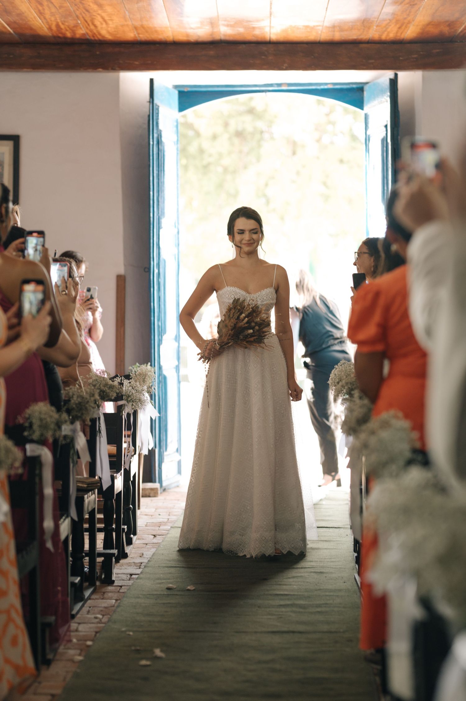 A bride wearing a strapless gown makes her entrance as guests watch from church pews.