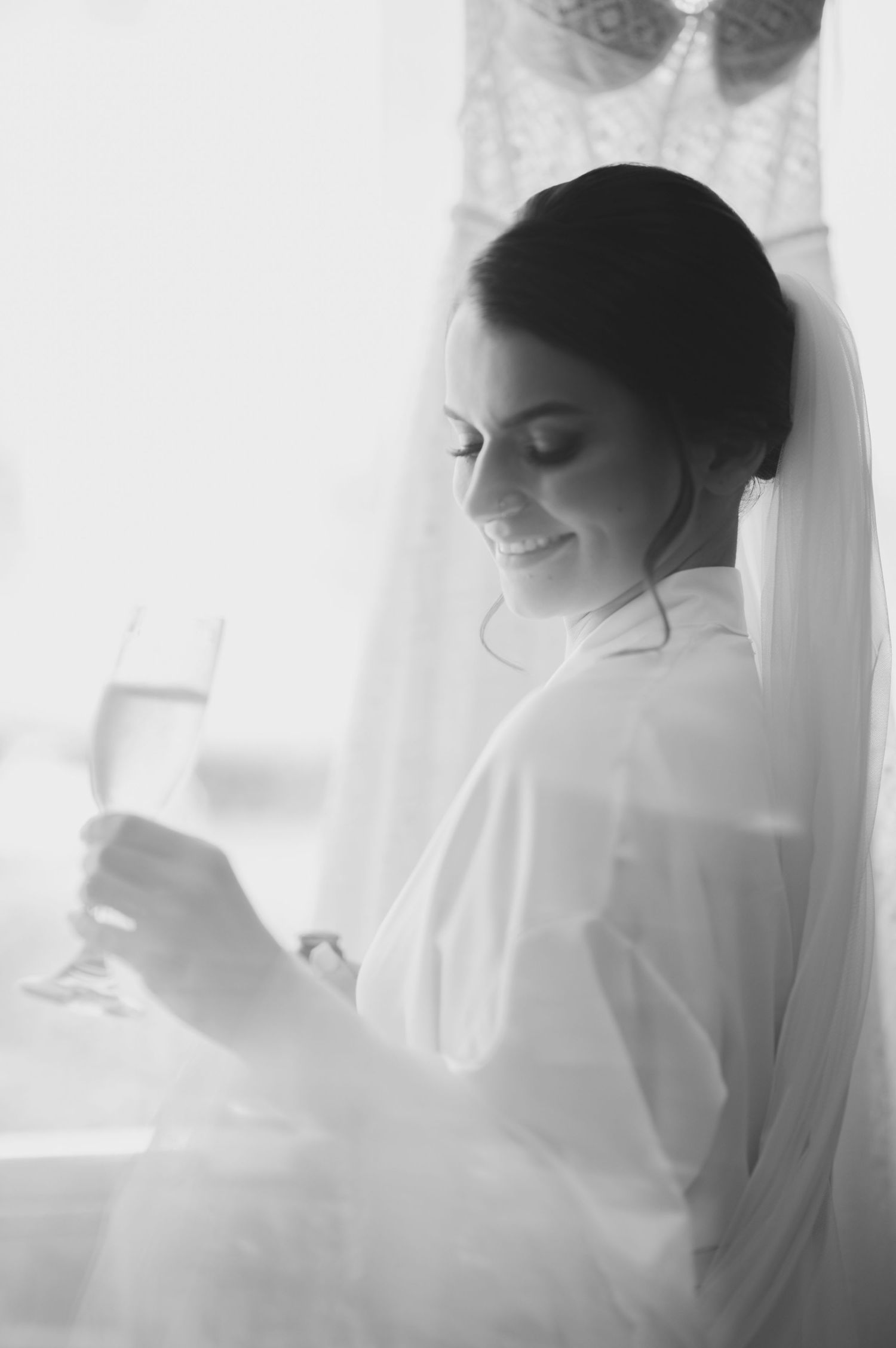 A black and white candid moment of bridal preparation with soft window light.