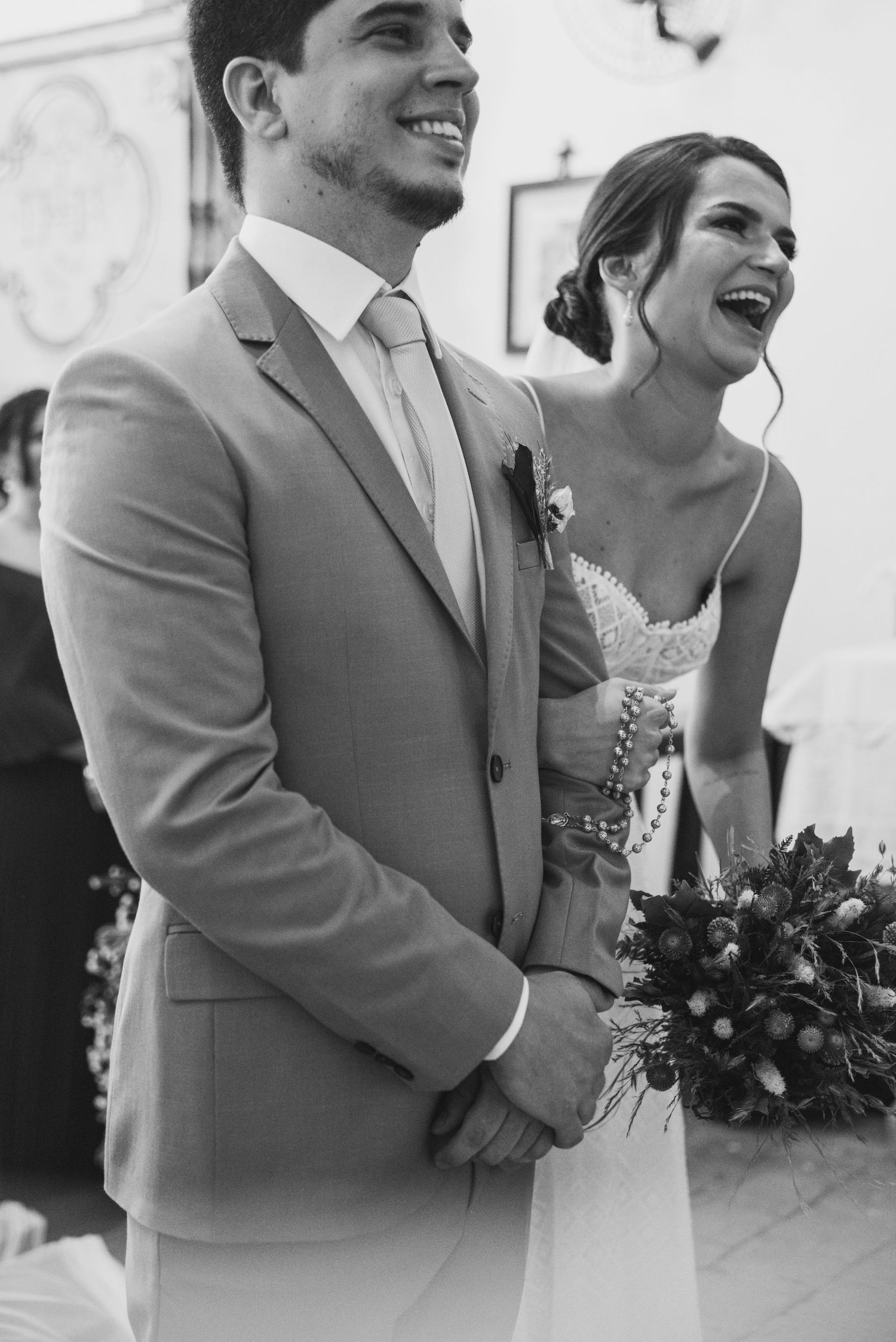 A black and white candid moment of newlyweds sharing laughter during their ceremony.