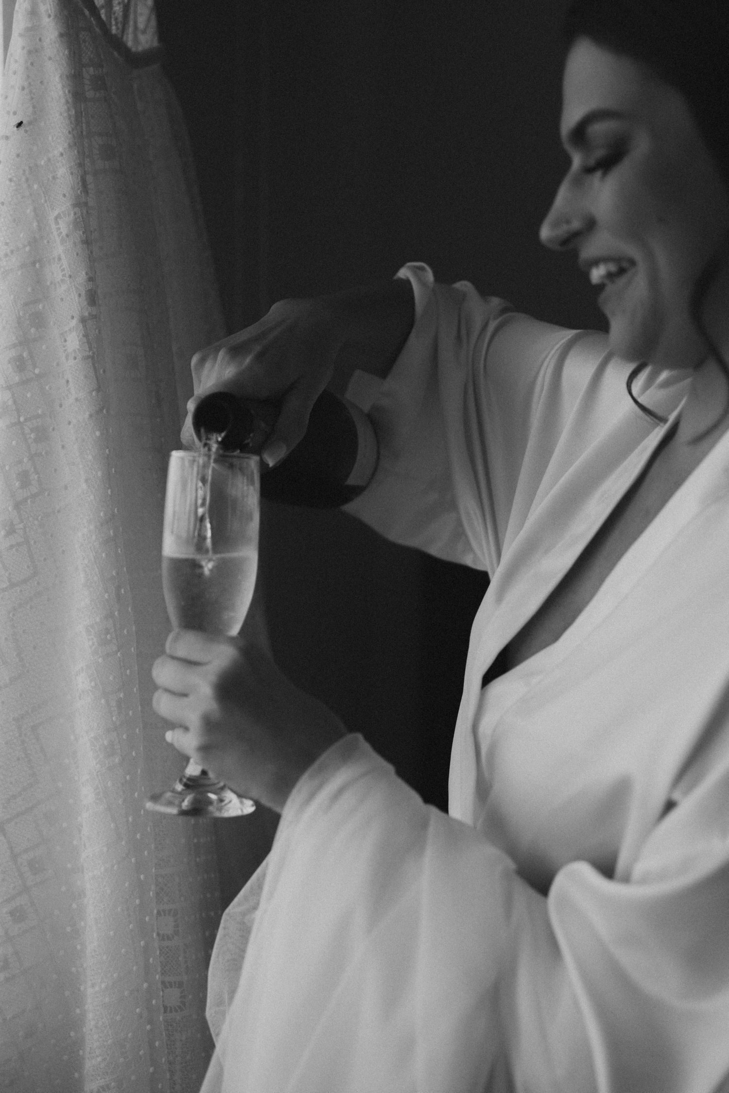 A black and white image of champagne being poured during wedding preparations.