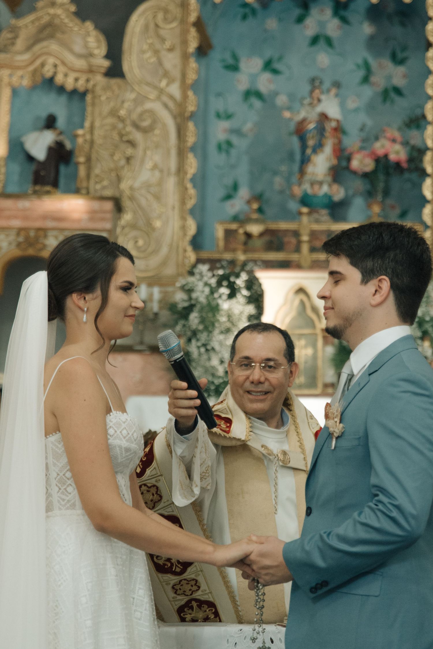 A wedding ceremony in progress with a priest officiating in front of an ornate church altar.