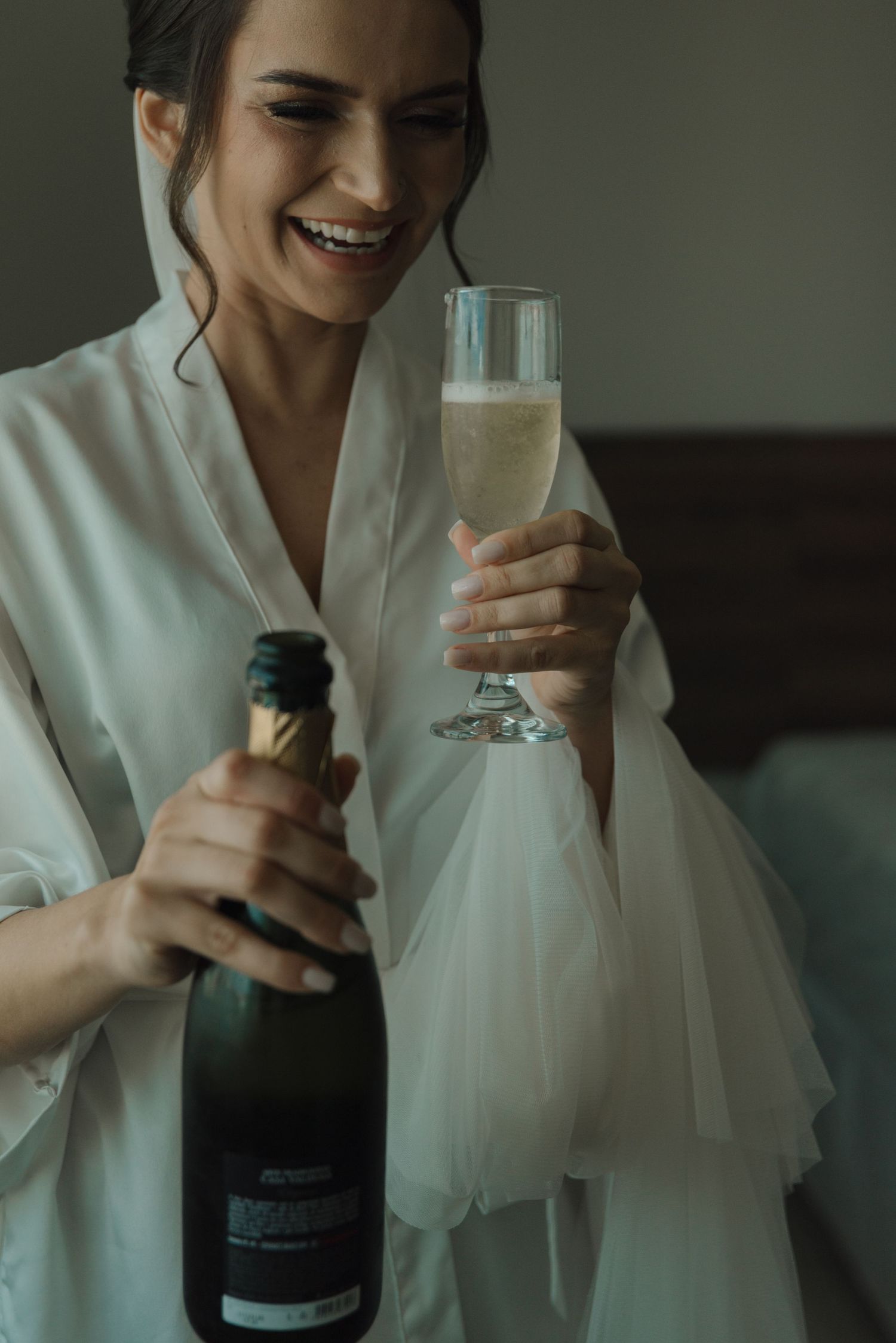 A person in a white robe toasts with a glass of champagne while holding the bottle.