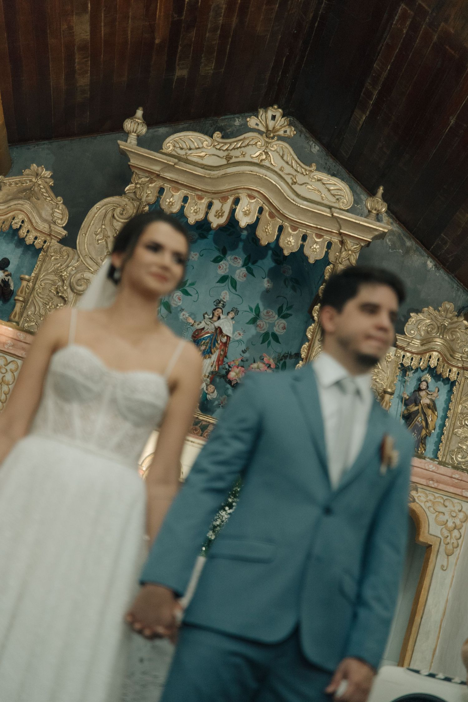 A couple stands before an ornate baroque altar with turquoise details during their wedding ceremony.