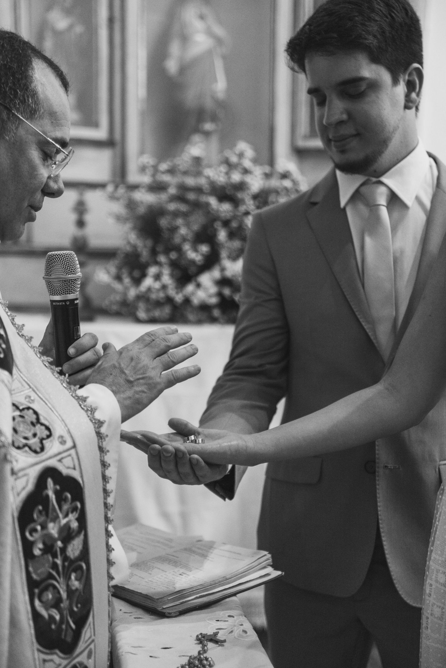 A black and white photo of a priest blessing a ring during a wedding ceremony.