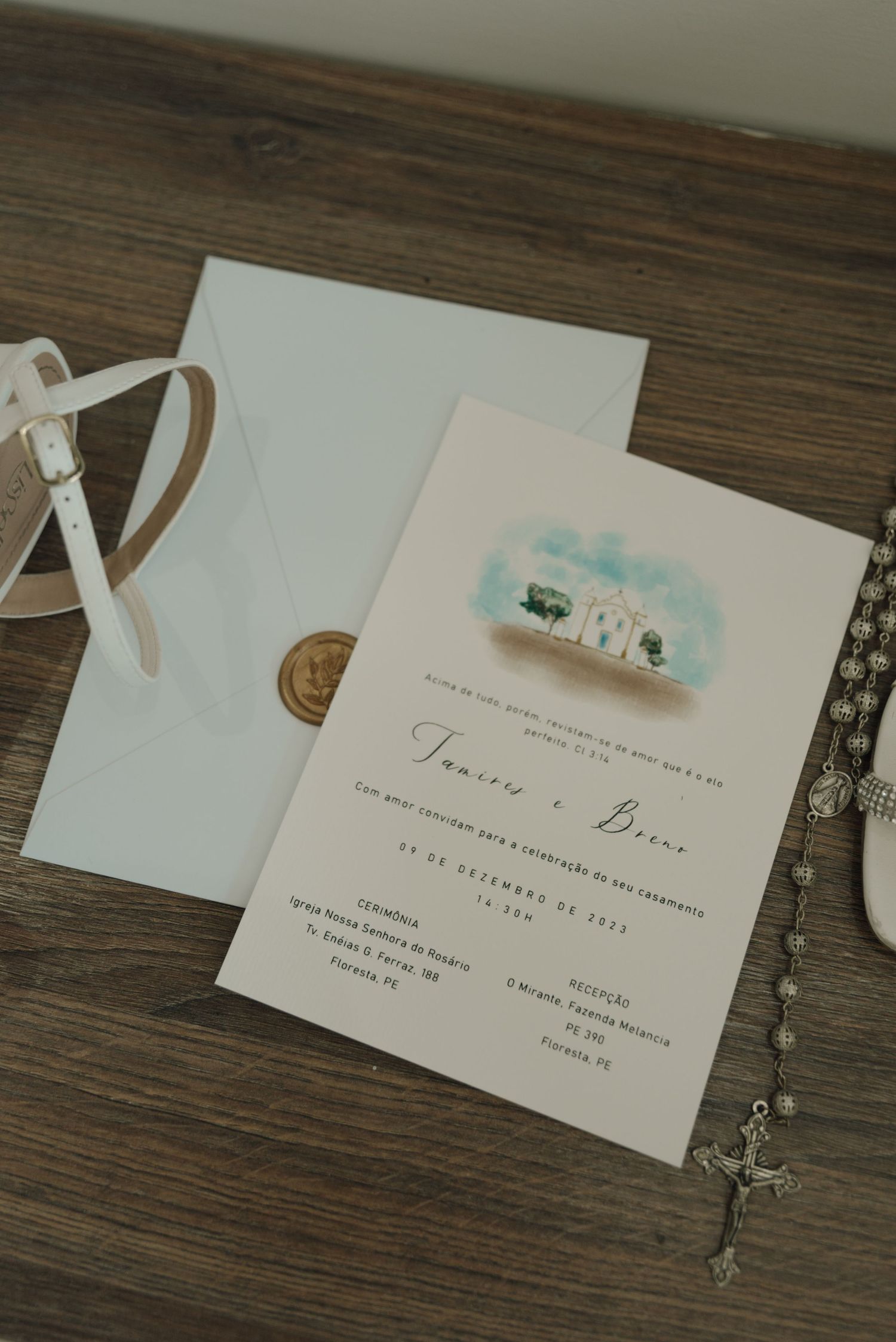Wedding invitation with watercolor design on wooden surface alongside decorative elements.