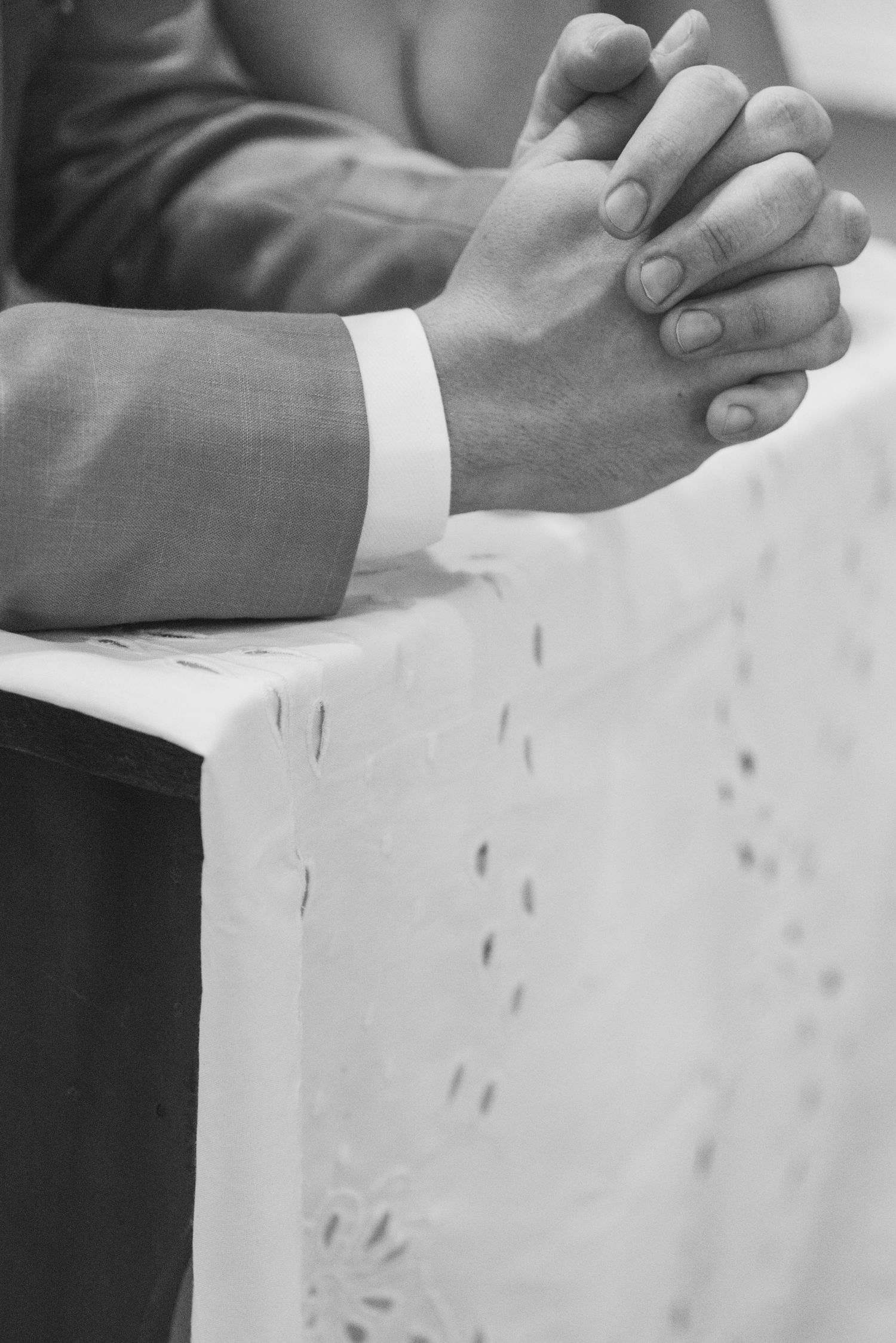 Close-up black and white shot of clasped hands in prayer position on a white tablecloth.