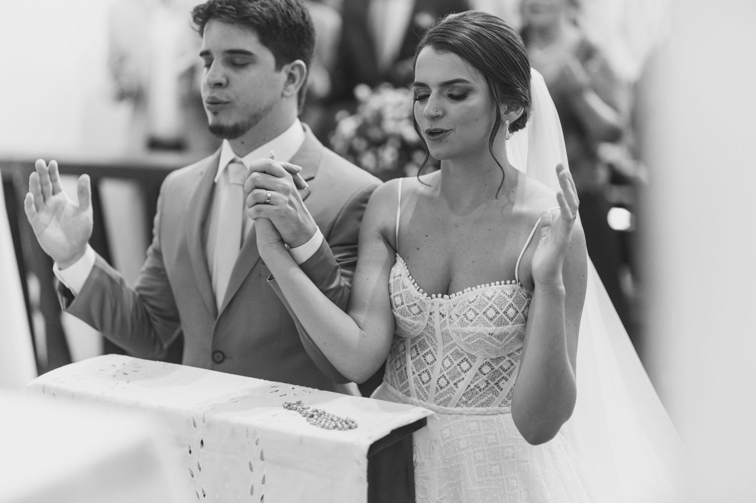 A couple in wedding attire praying together during their ceremony in black and white.