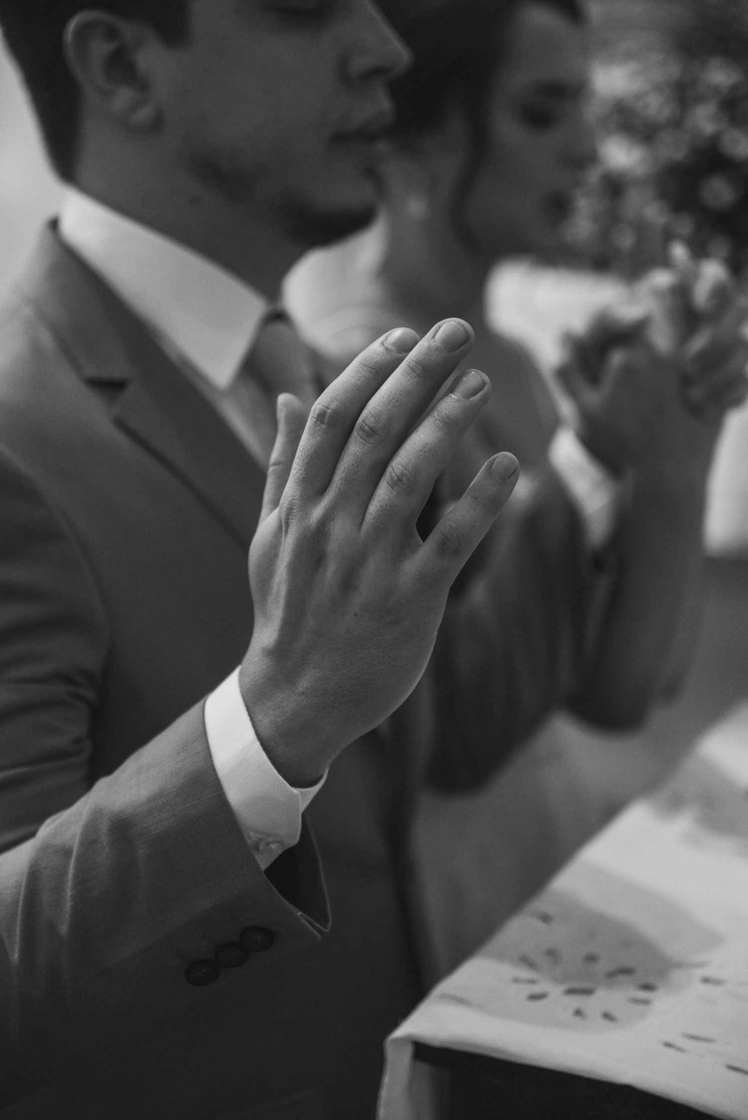 Black and white image of hands clasped in prayer during a wedding ceremony.
