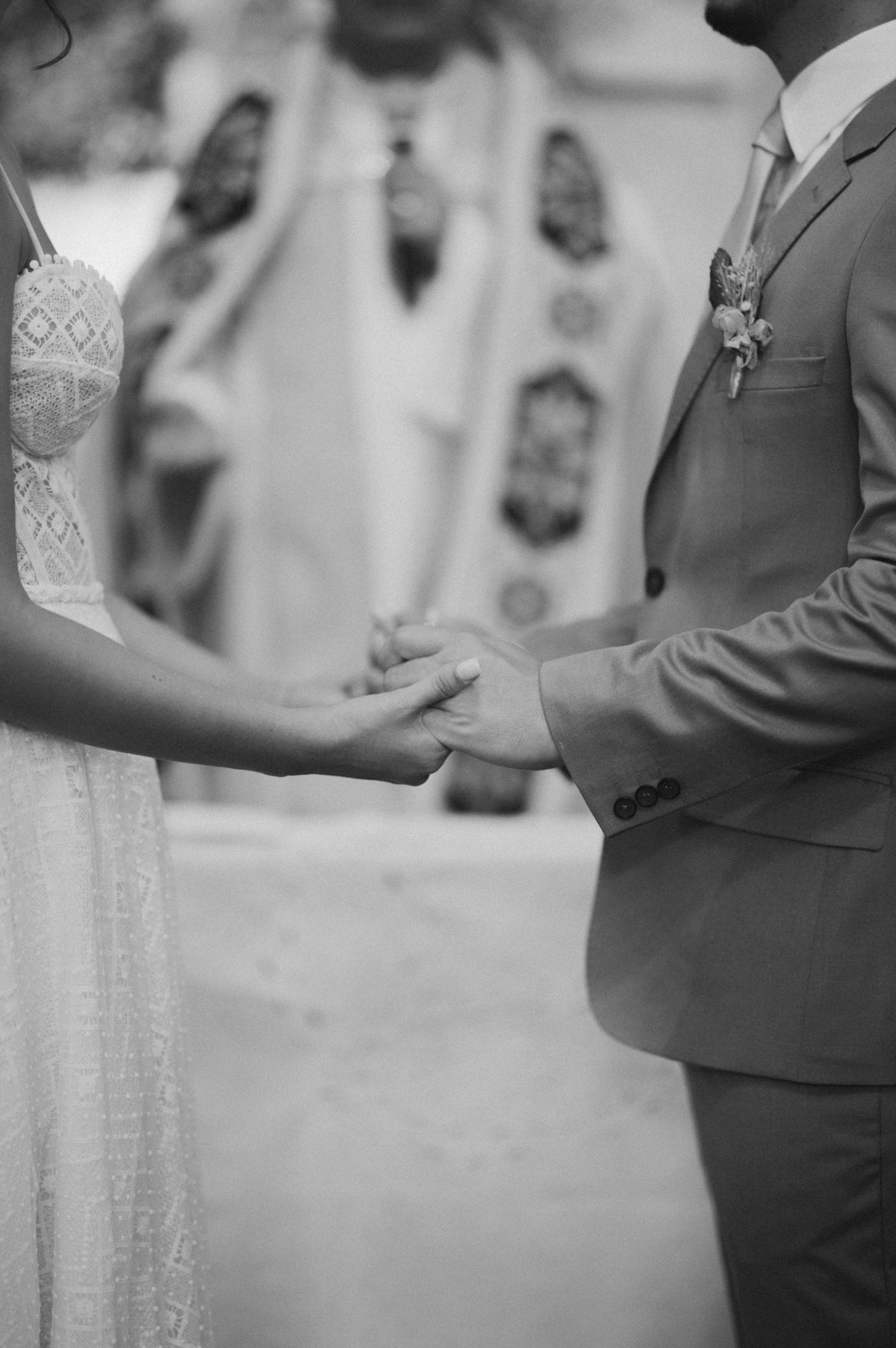 Black and white photo of a couple holding hands during their wedding ceremony.