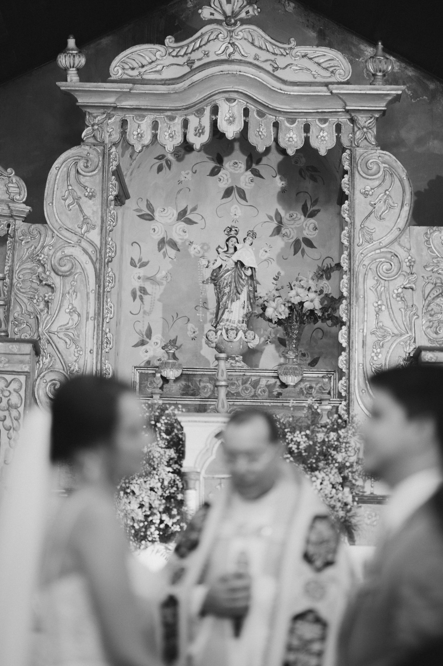 A wedding ceremony in front of an ornate religious altar decorated with flowers.