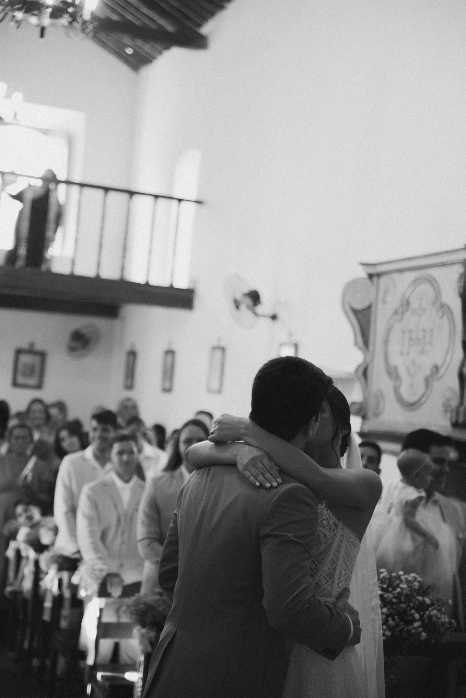 A black and white photograph captures a tender embrace during a wedding ceremony in a church.