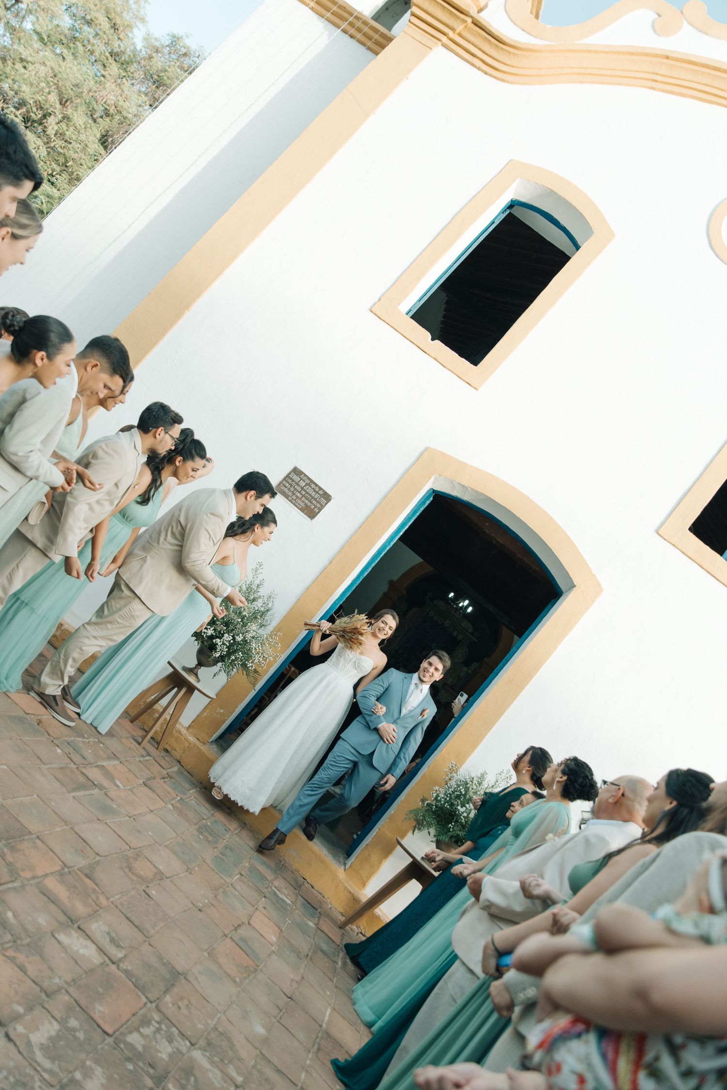 Wedding party in mint green dresses gathers outside a white colonial church building.