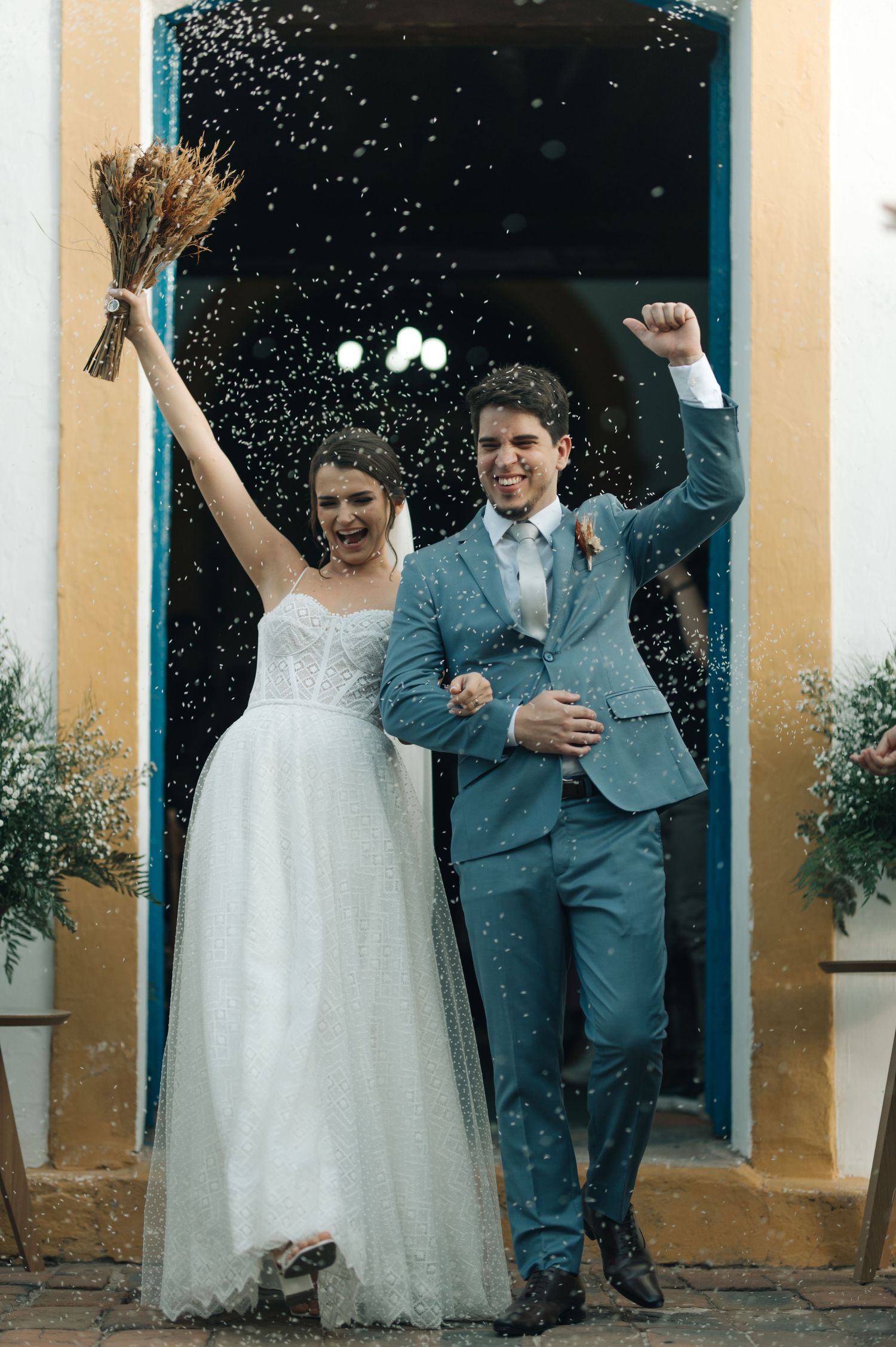 Happy couple celebrates with raised arms amid confetti shower outside church entrance.