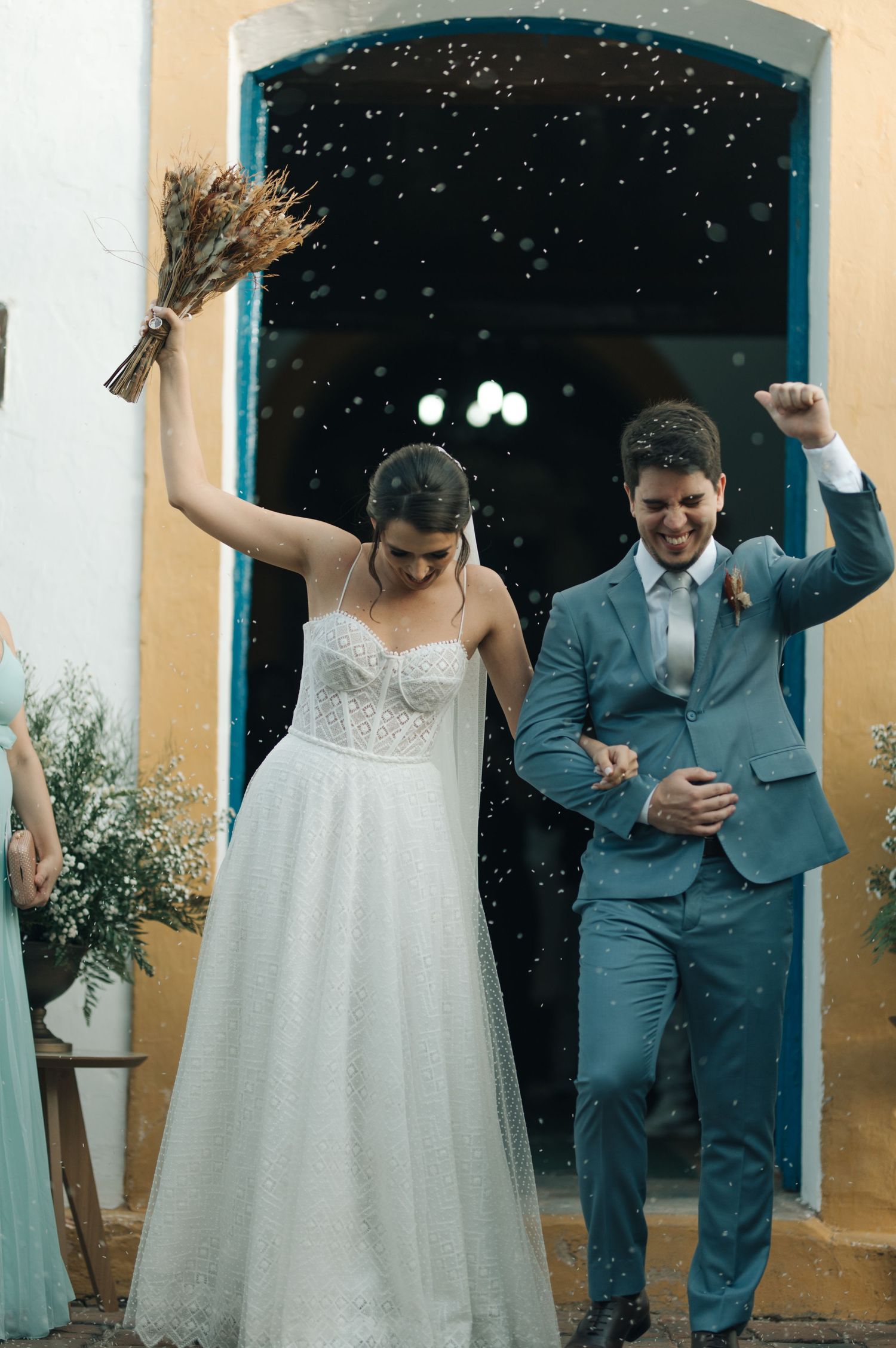 Jubilant newlyweds celebrate with raised arms amidst falling confetti outside church doors.
