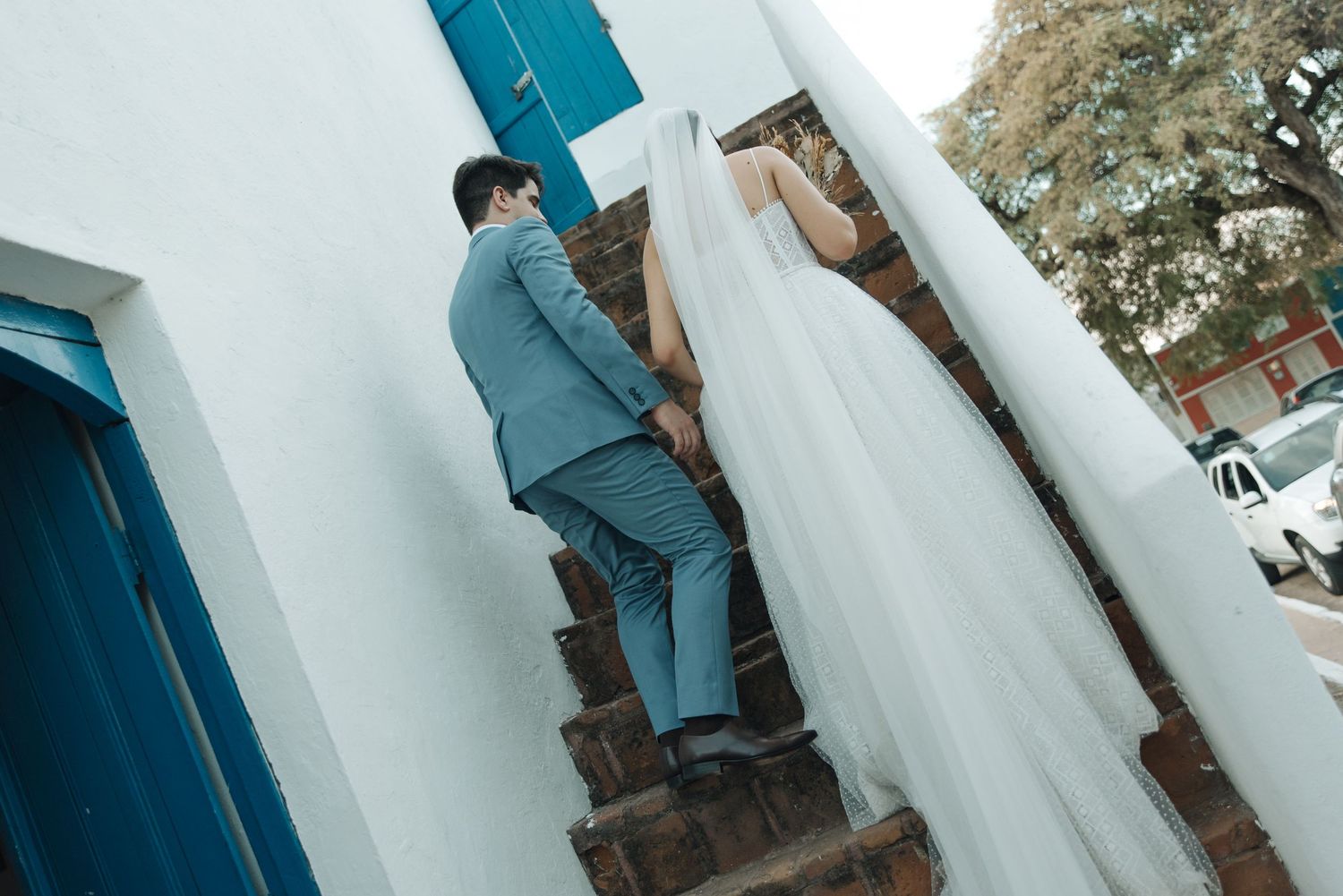 Couple ascending white staircase with blue accents during wedding photoshoot.