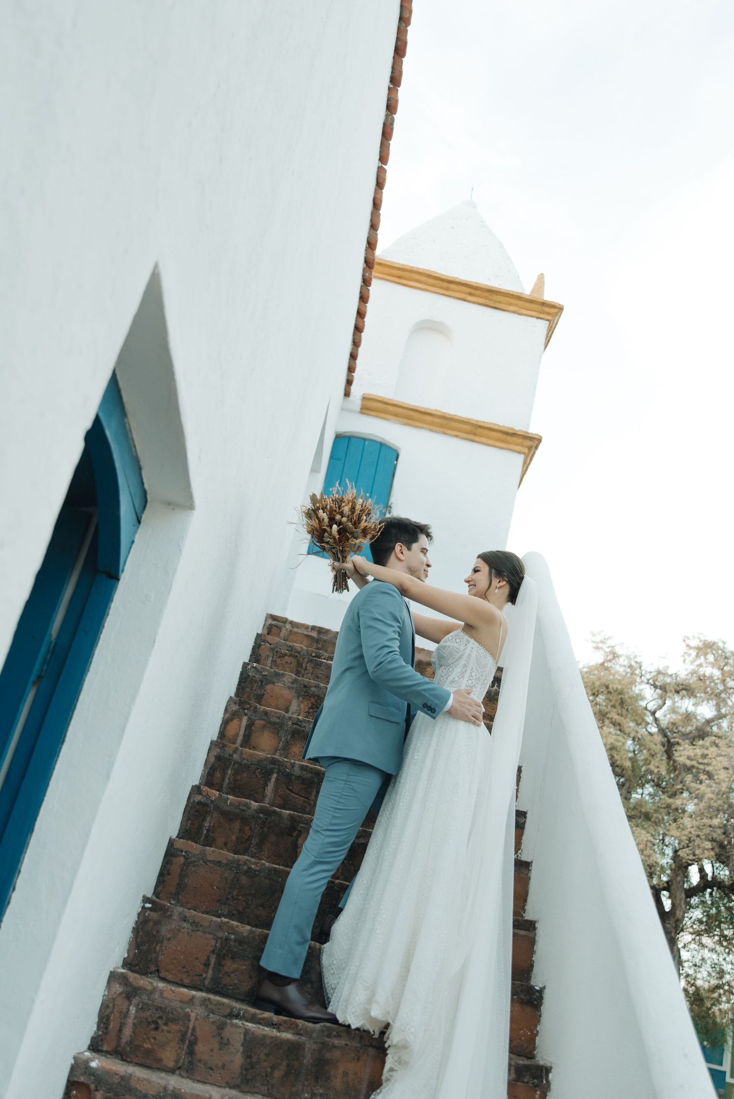 Romantic moment captured on brick stairs with white walls and blue accents.
