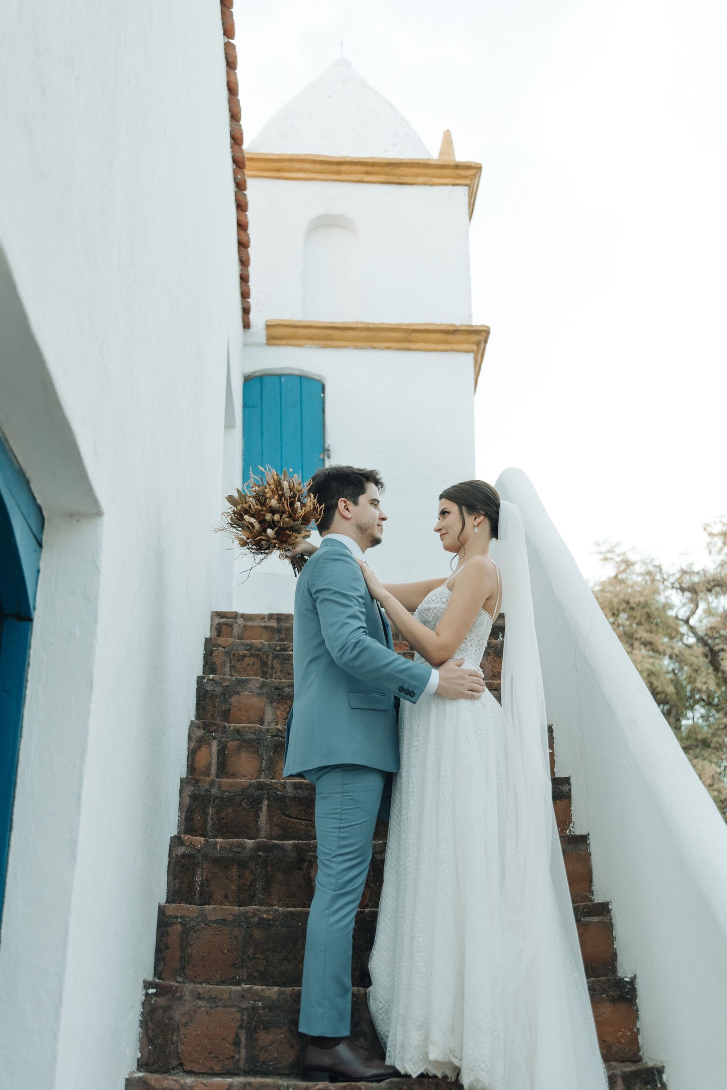 Wedding couple shares intimate moment on rustic steps with white church architecture.