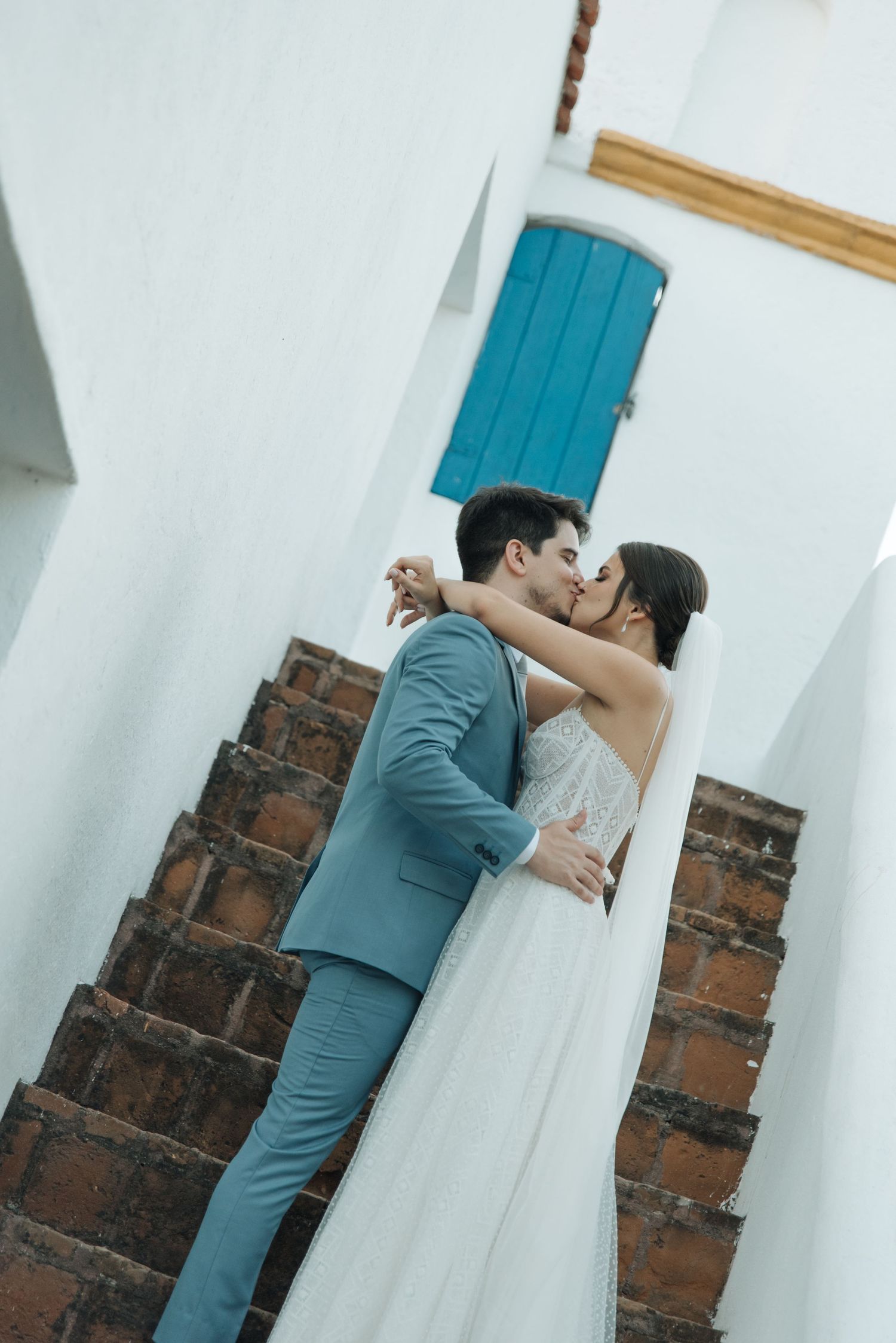 Romantic wedding portrait on rustic steps with blue door and white architecture.