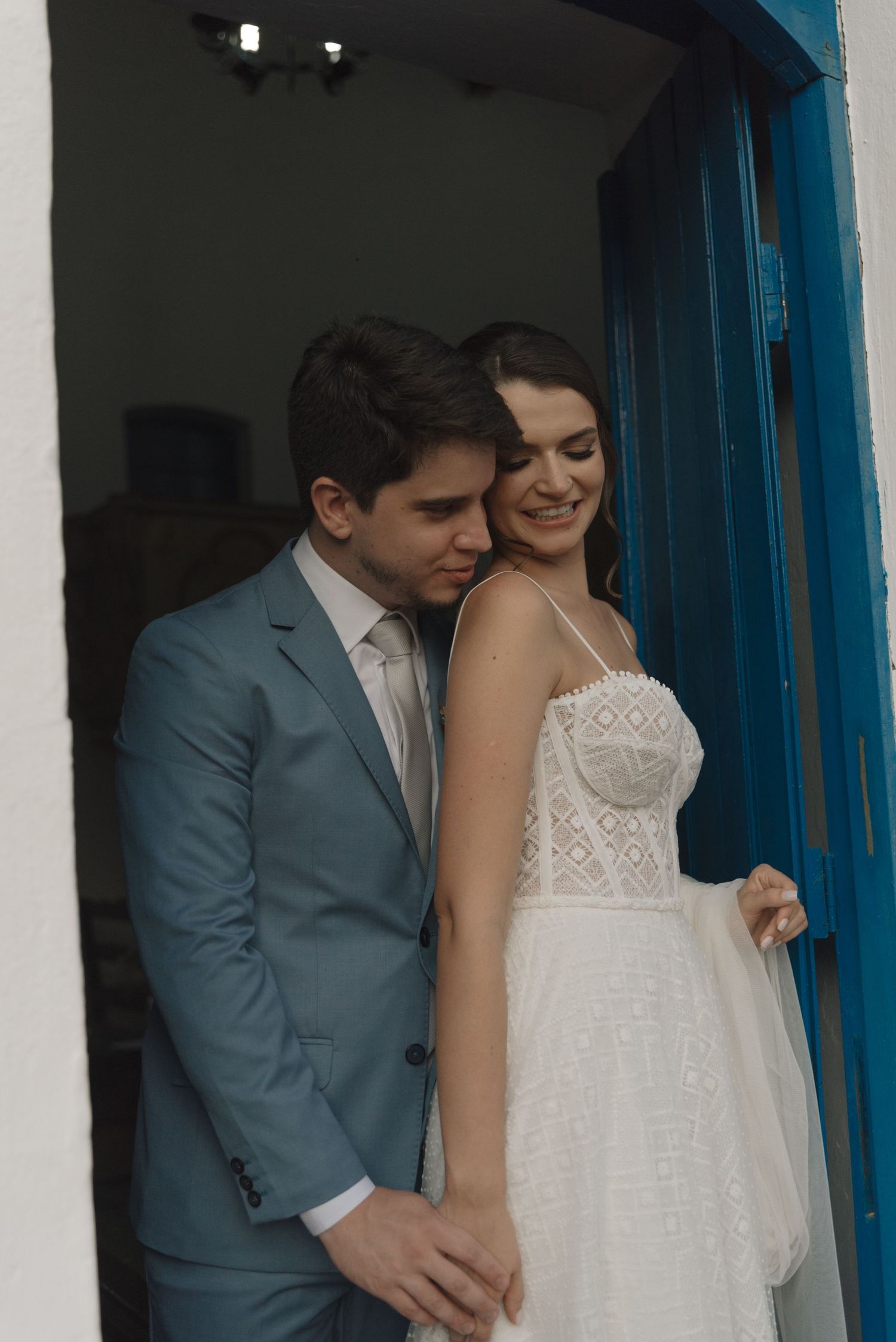 Romantic wedding couple poses in doorway with bright blue trim and white walls.