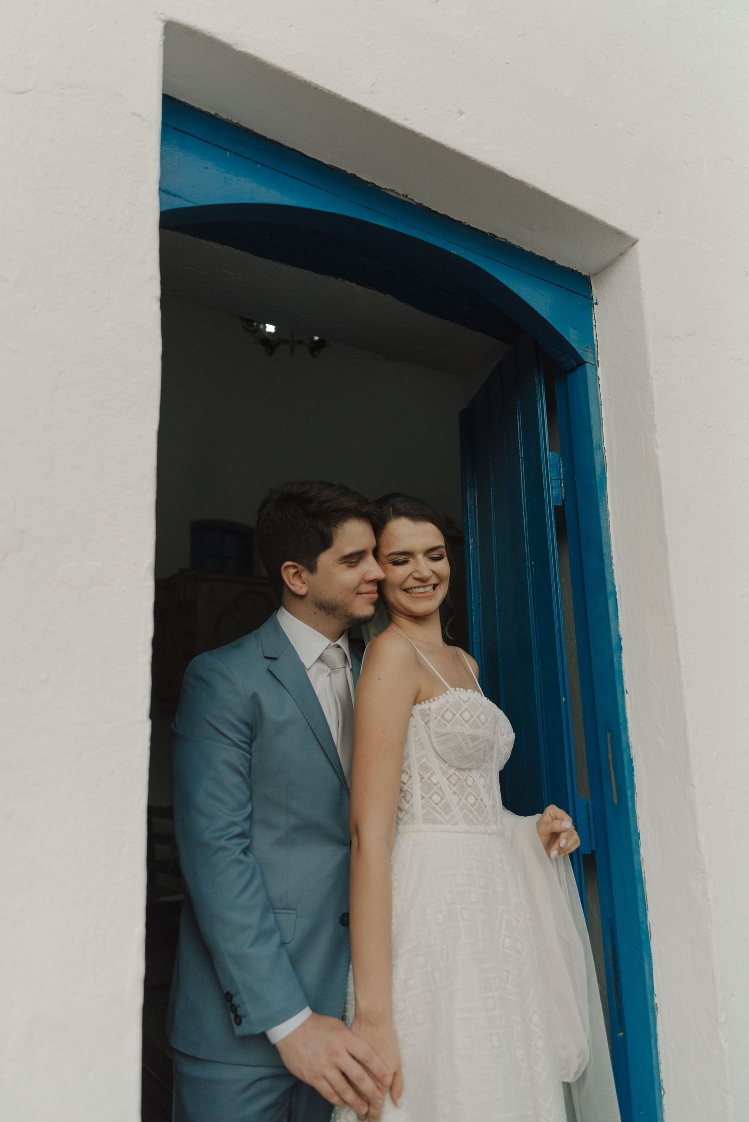 Wedding couple shares joyful moment in archway with traditional Mediterranean architecture.