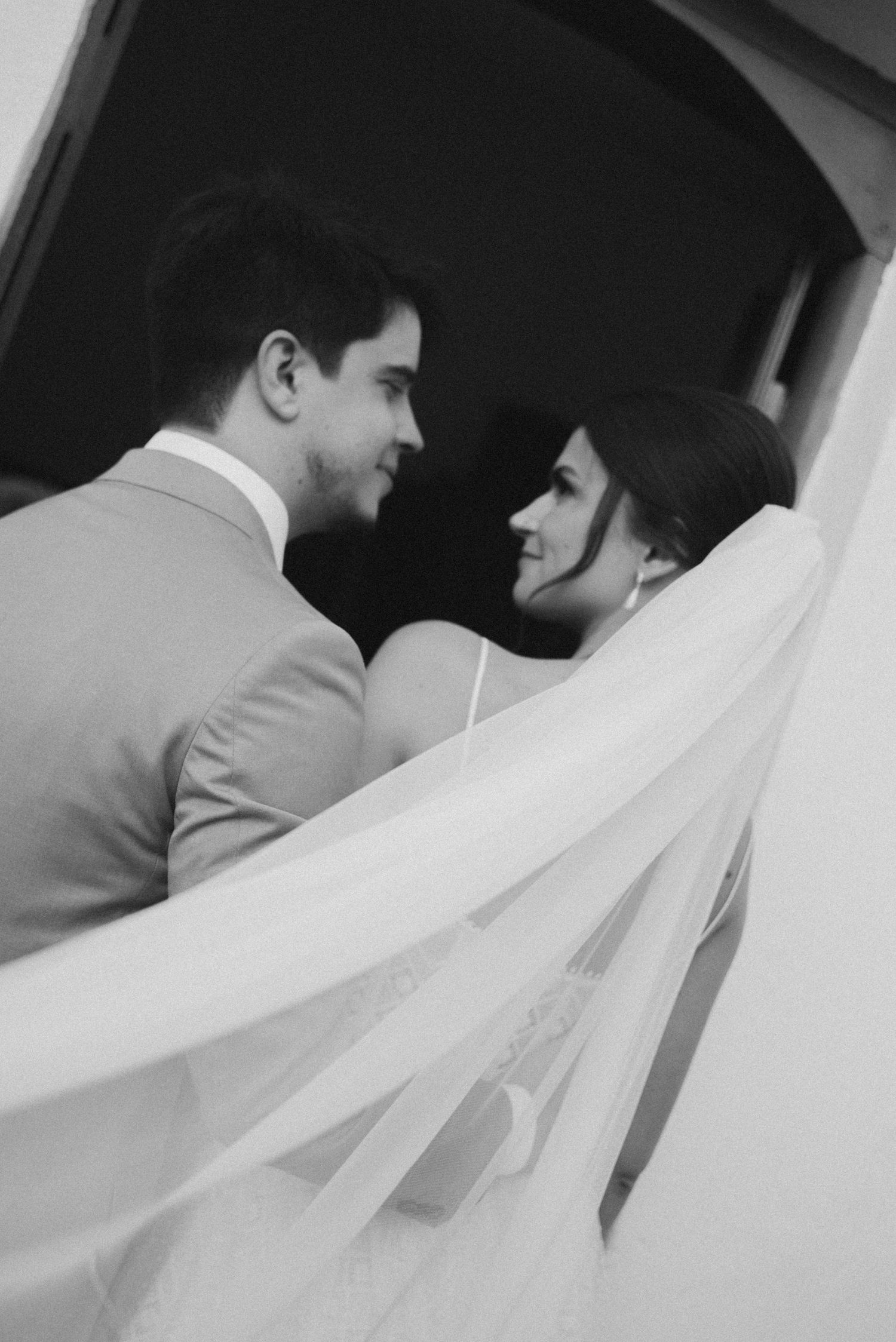 Black and white portrait of wedding couple with flowing veil in doorway.