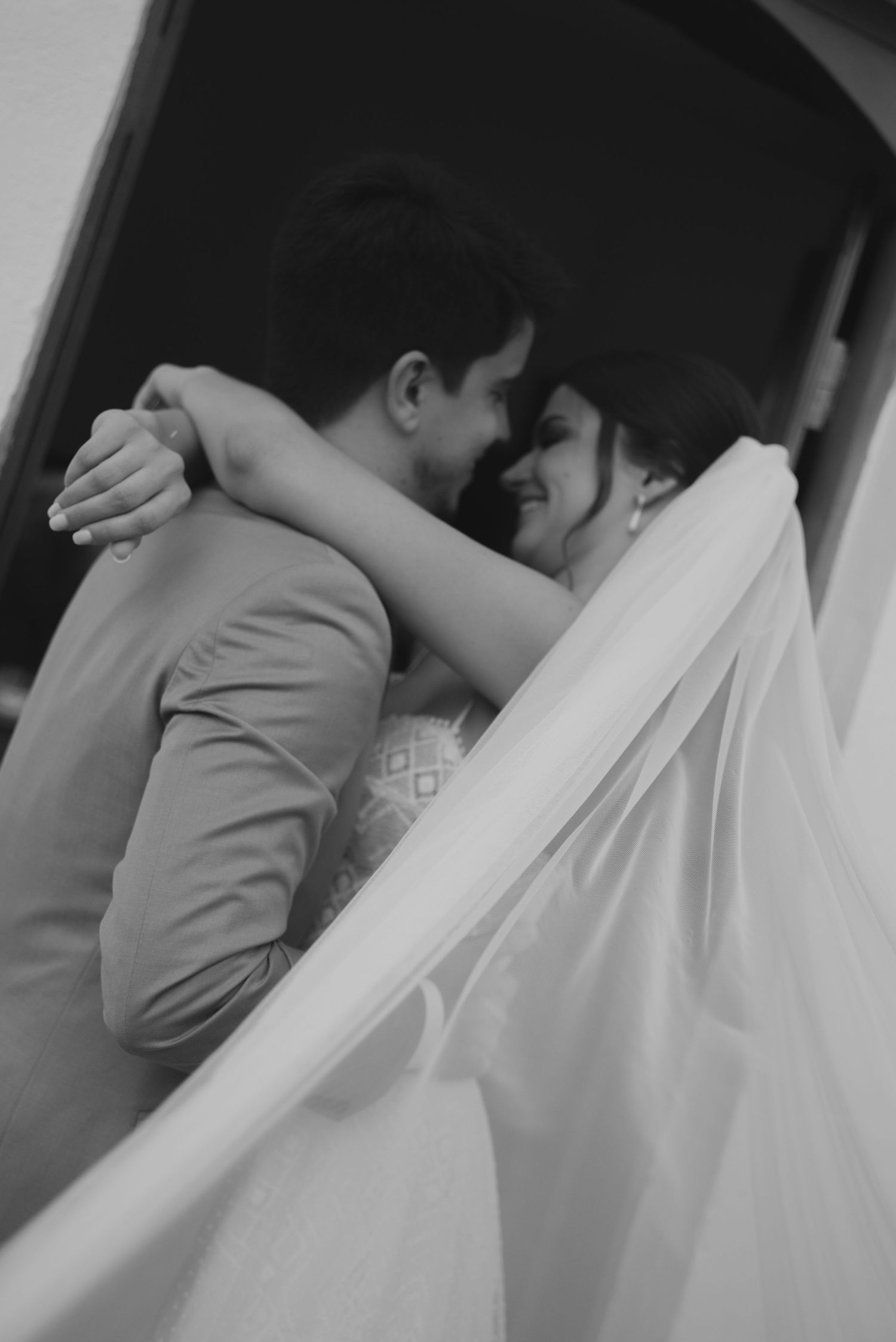 Artistic black and white shot of newlyweds embracing with flowing veil.