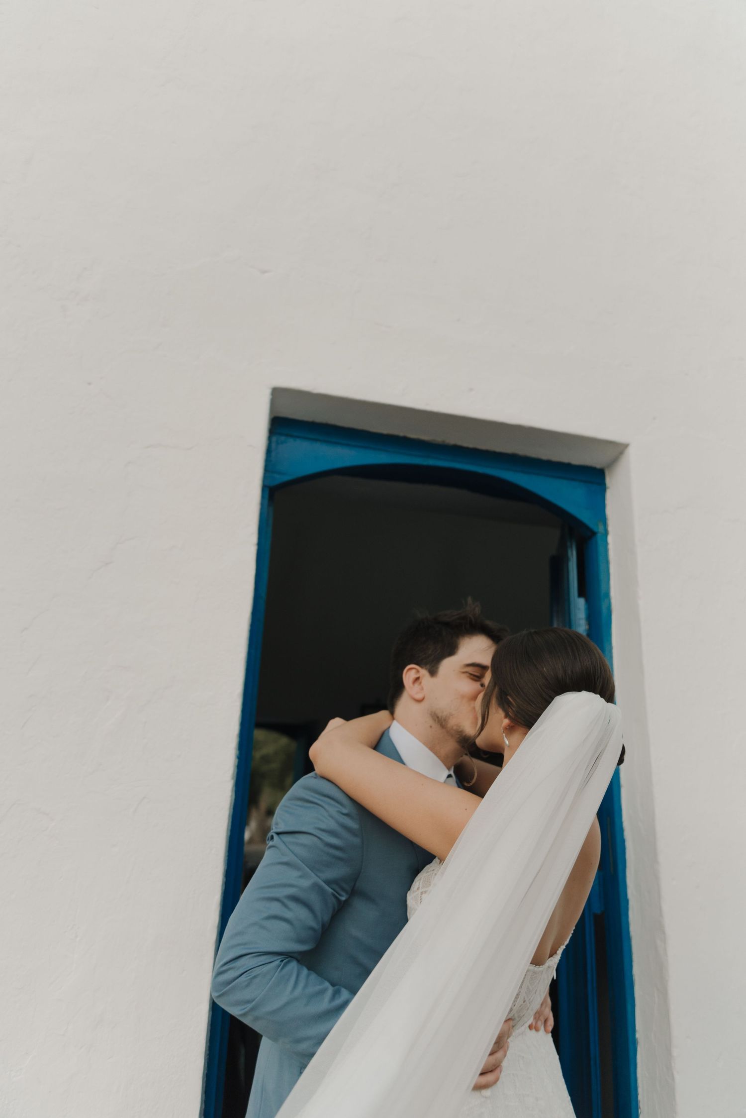 Intimate wedding portrait framed by blue doorway against white Mediterranean architecture.