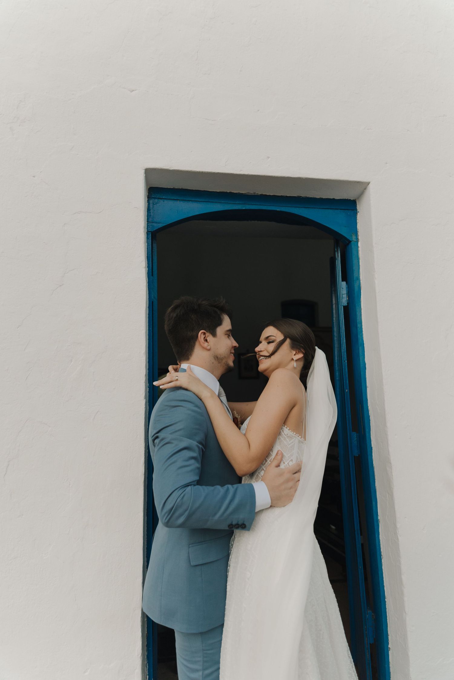 A romantic wedding moment captured in a blue-framed doorway of a white building.