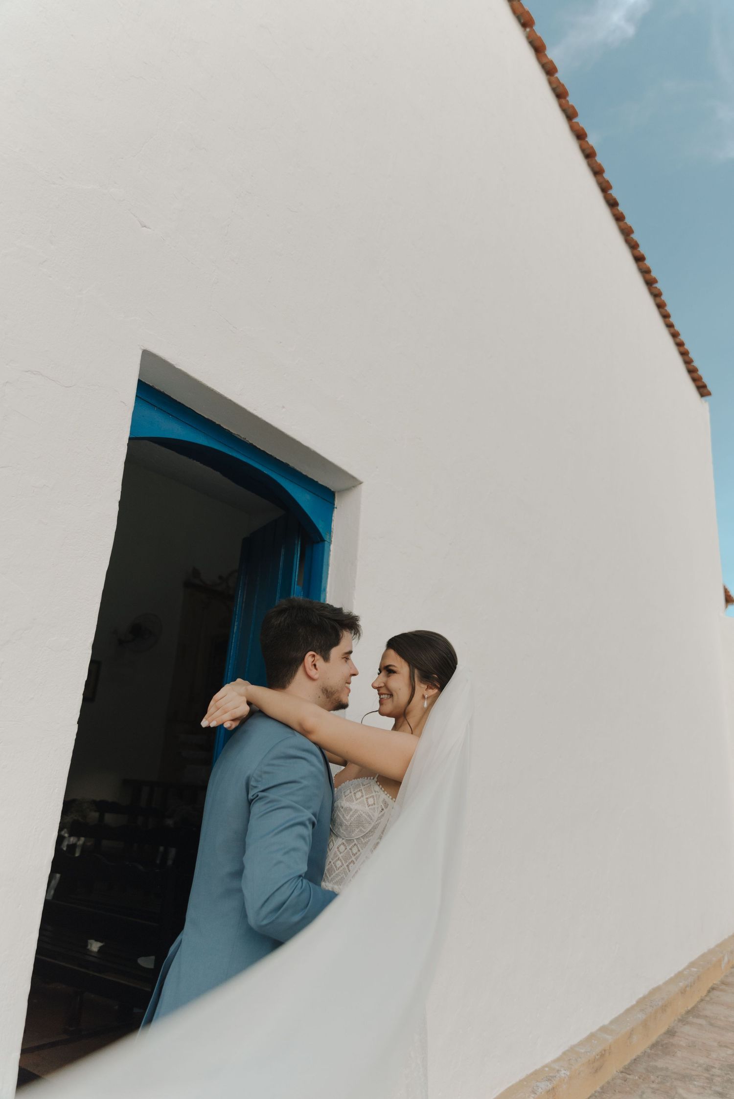 A tender embrace between newlyweds in a white doorway with blue trim.