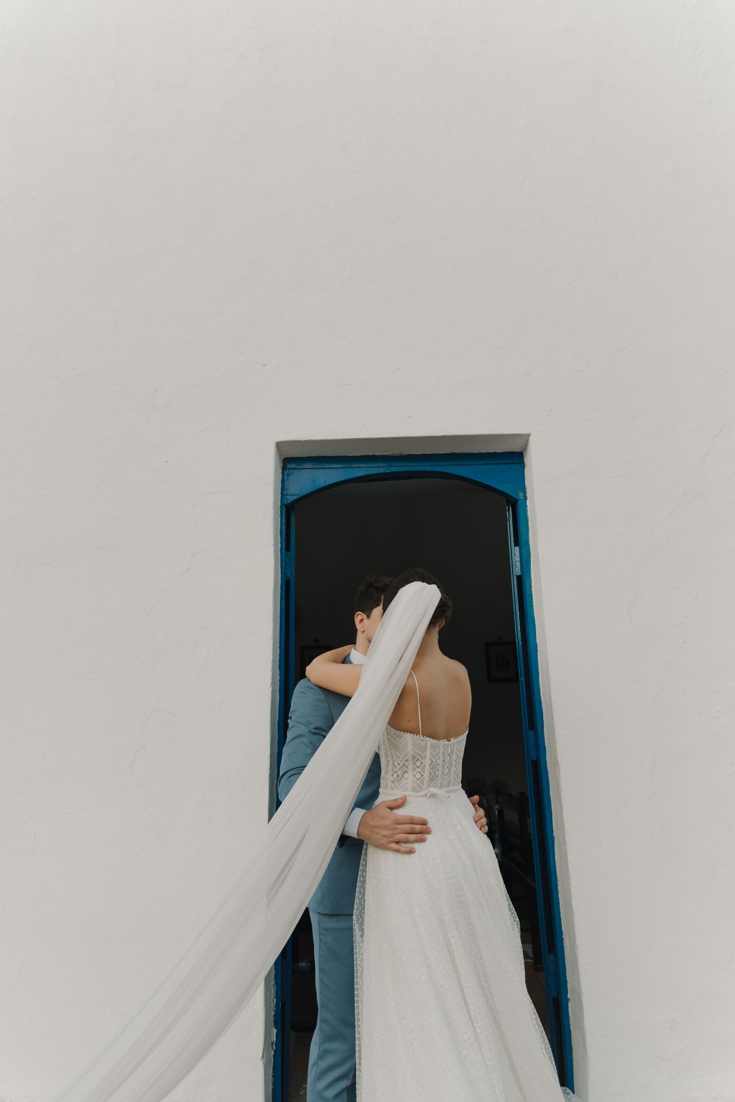 An artistic overhead shot of newlyweds with flowing veil in a blue-framed doorway.