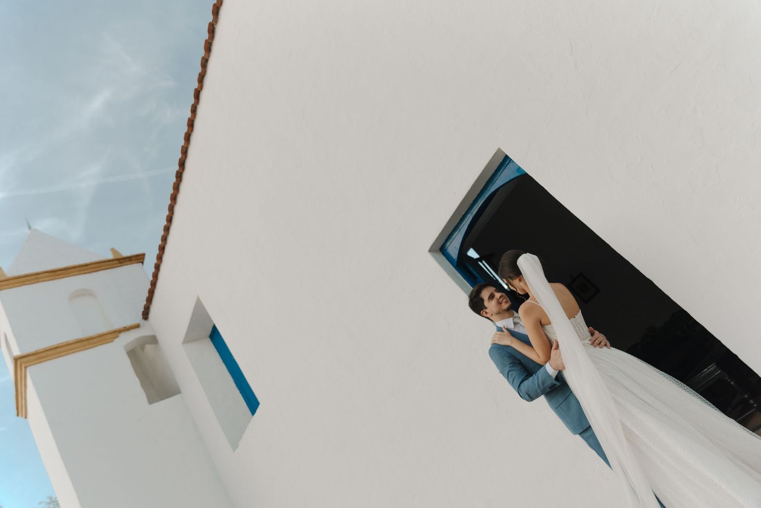 An upward architectural view of newlyweds in a dramatic doorway with flowing veil.