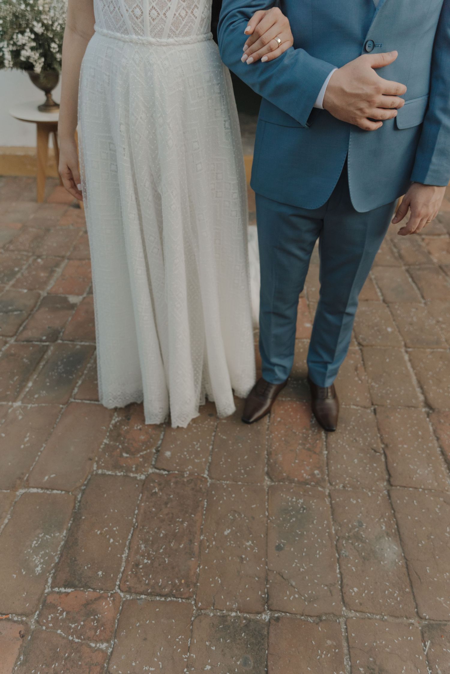 Detail shot of wedding attire showing blue suit and white dress against brick pavement.