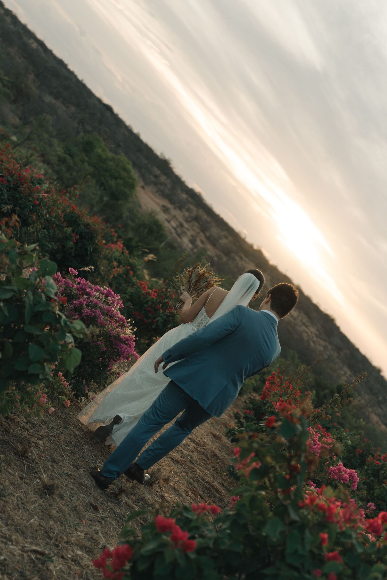 A sunset wedding portrait among coastal flowers and mountain scenery.
