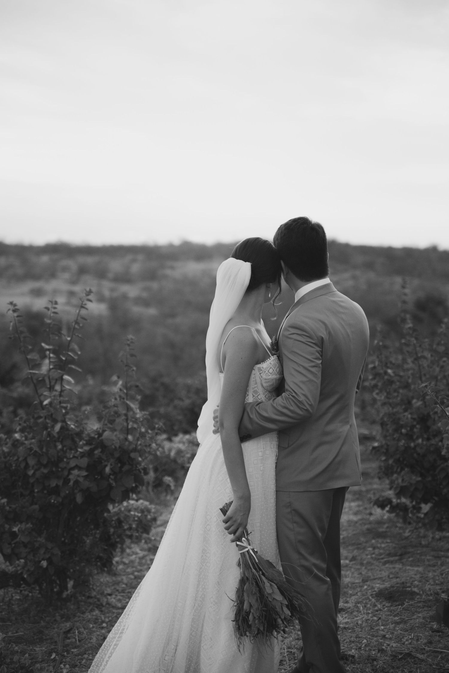 A black and white photo captures a tender moment between newlyweds in a desert garden.