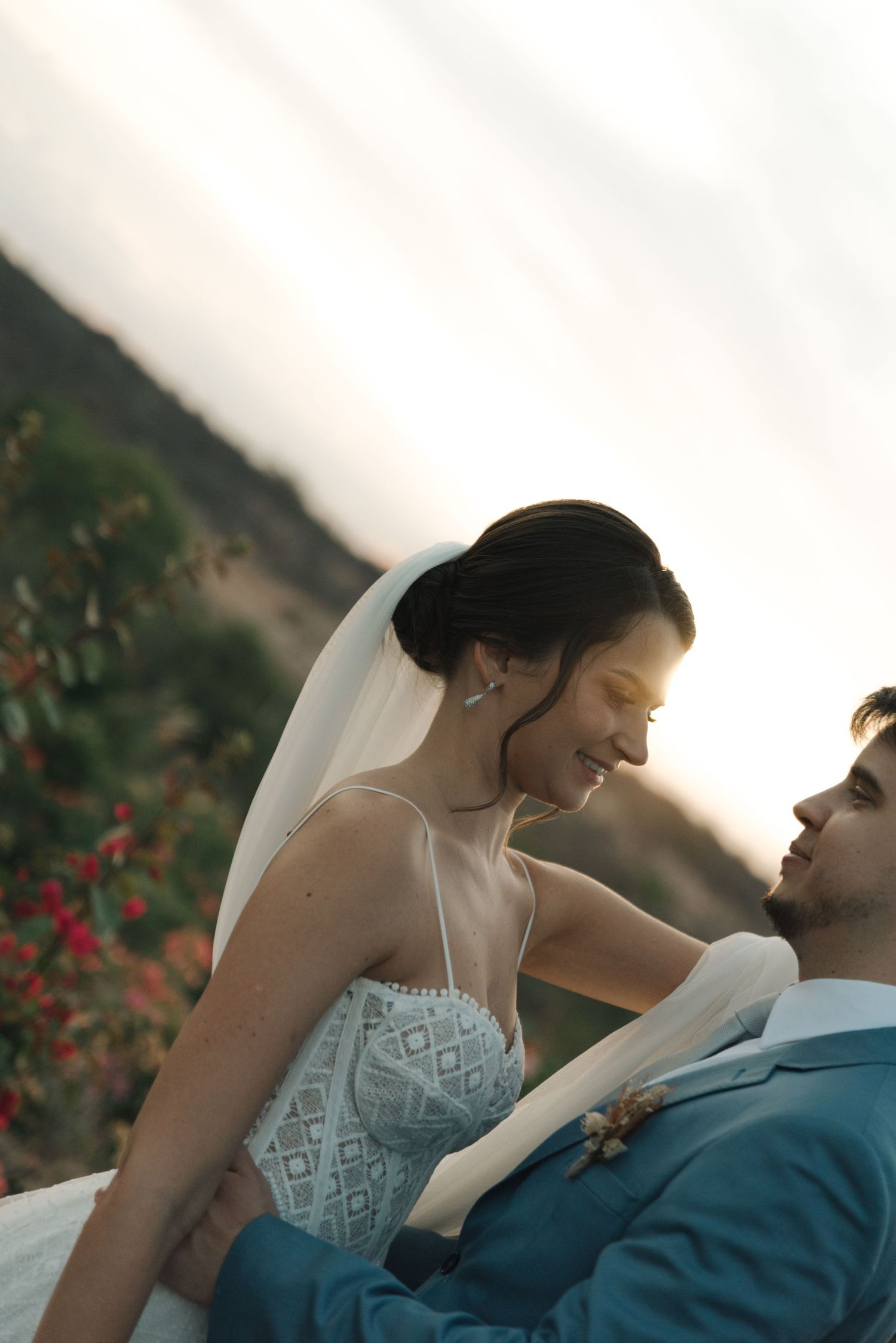 Intimate moment between newlyweds with bride in lace dress and groom in blue suit at sunset.