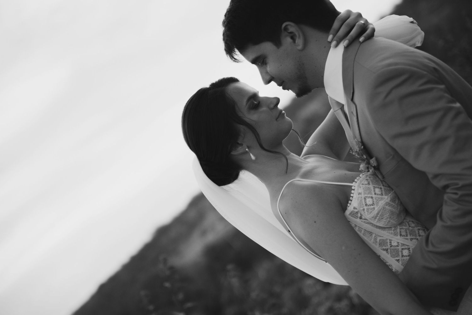 Romantic black and white portrait of a couple in wedding attire sharing a close embrace.