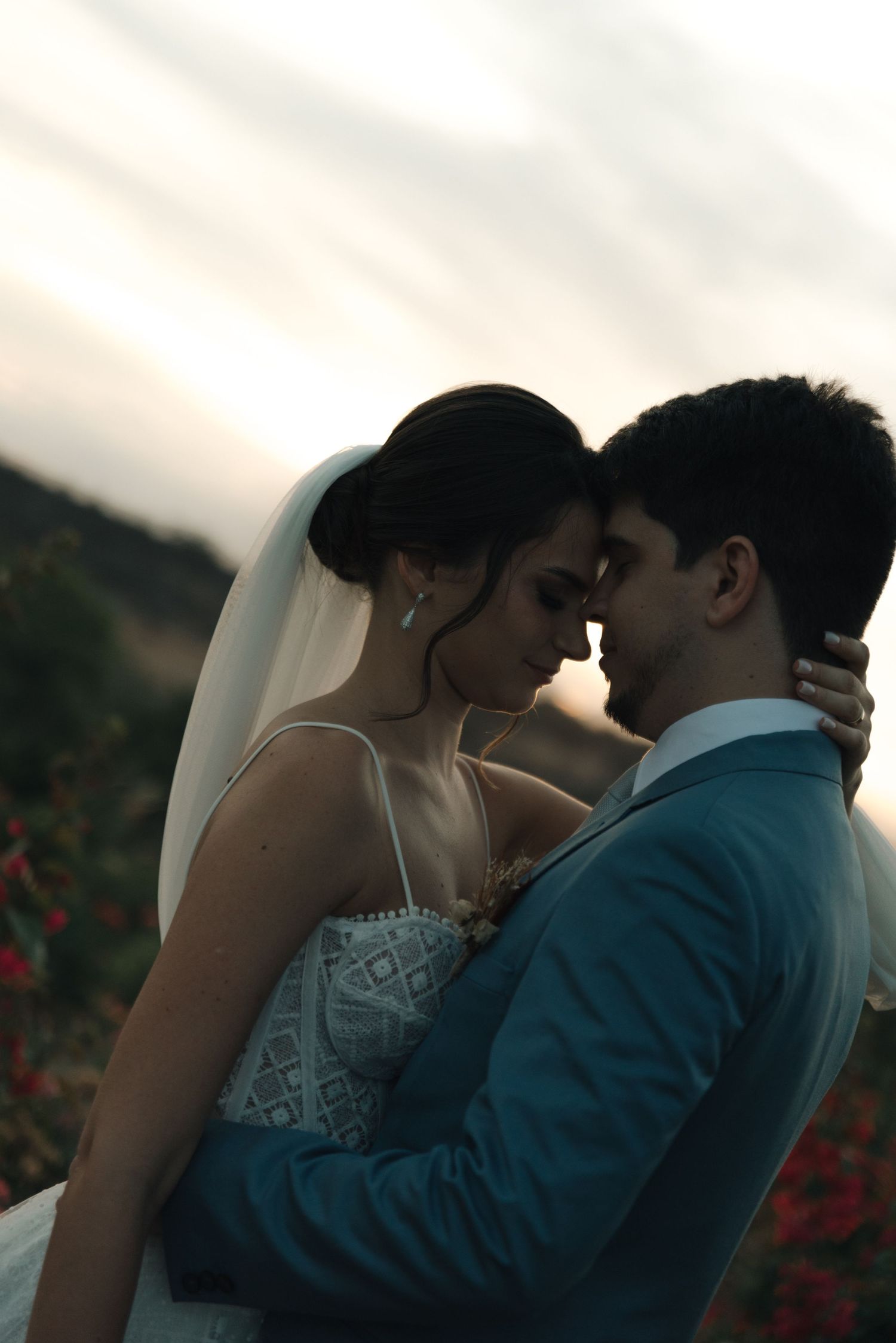 Wedding couple shares a tender moment among red flowers at golden hour.